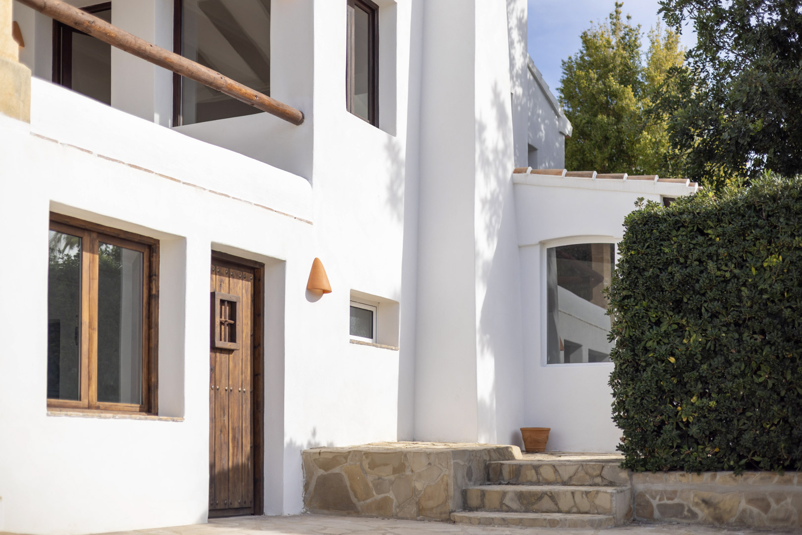 Façade de villa à Jávea avec détails rustiques : porte en bois, murs blancs et marches en pierre.