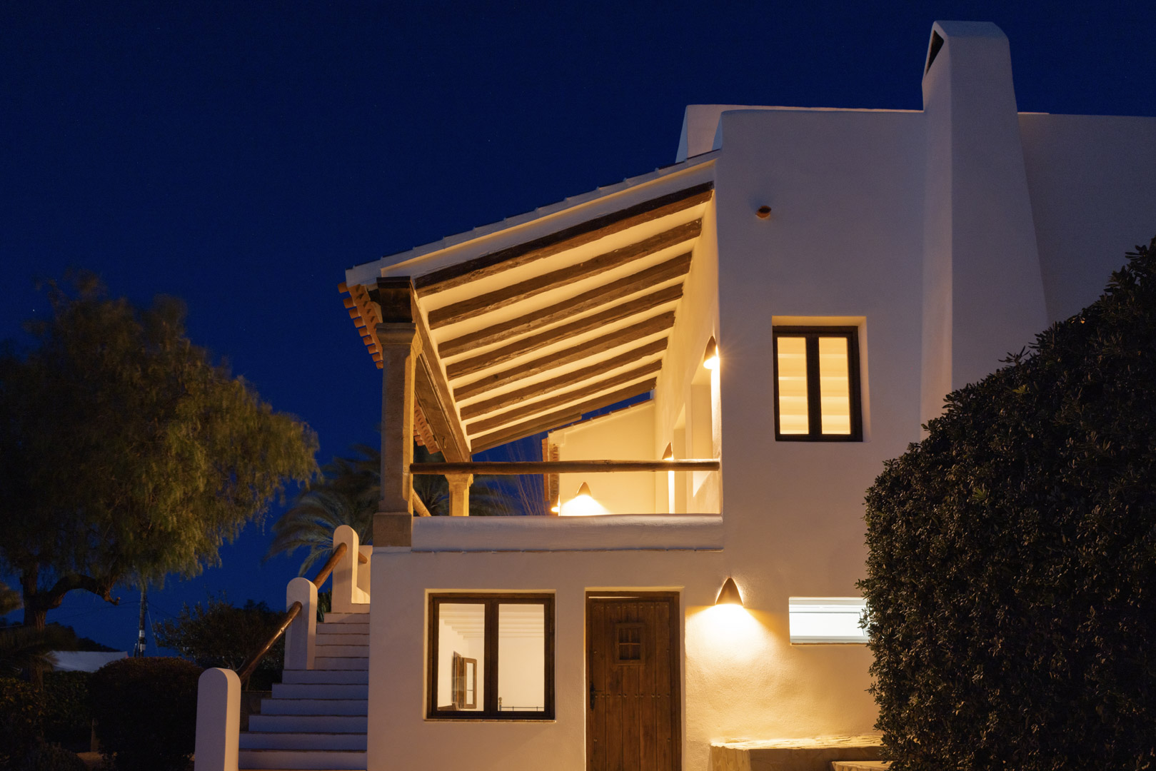 Façade illuminée de villa à Tosalet, Jávea. Architecture méditerranéenne avec terrasse couverte et détails en bois.