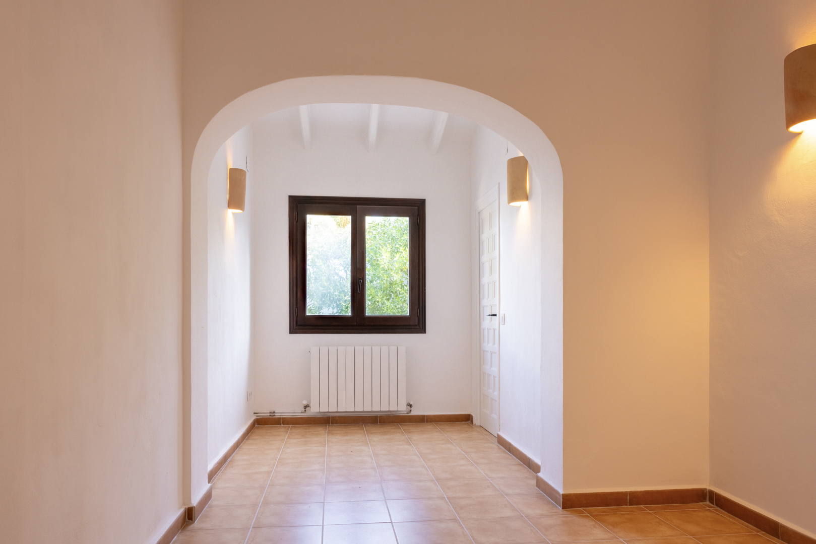 Intérieur lumineux avec arche architecturale, sol en céramique et fenêtre à cadre en bois foncé.