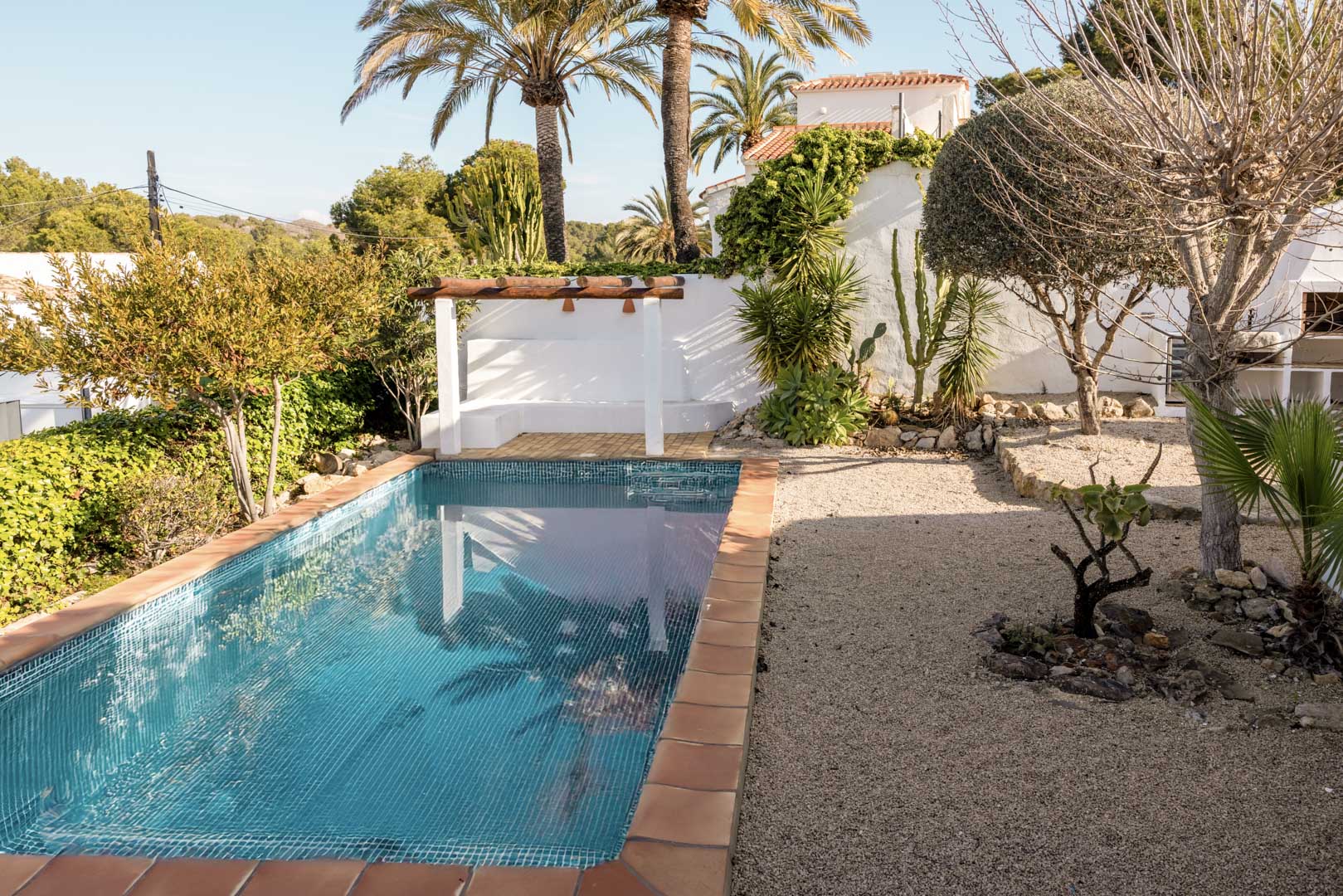 Piscine rectangulaire bordée de terre cuite et solarium ombragé par une pergola dans un jardin méditerranéen.