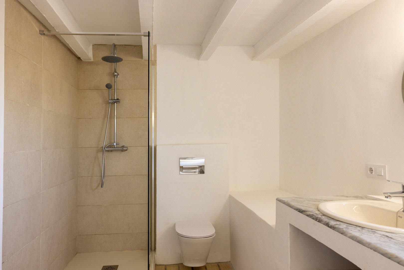 Salle de bain avec douche à l'italienne carrelée crème, toilettes blanches et lavabo avec comptoir en marbre.