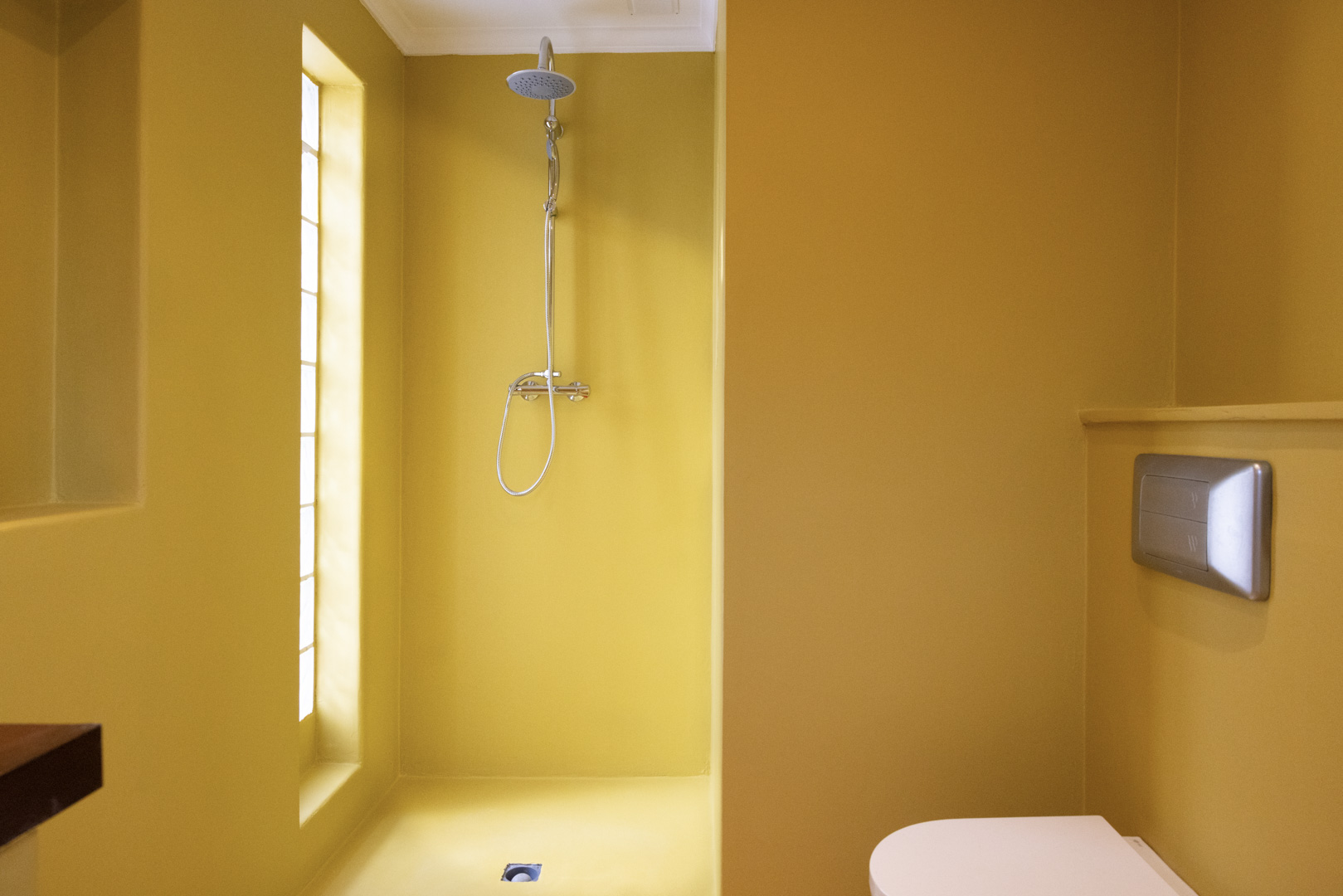 Salle de bain avec murs couleur moutarde, douche en acier et fenêtre verticale.