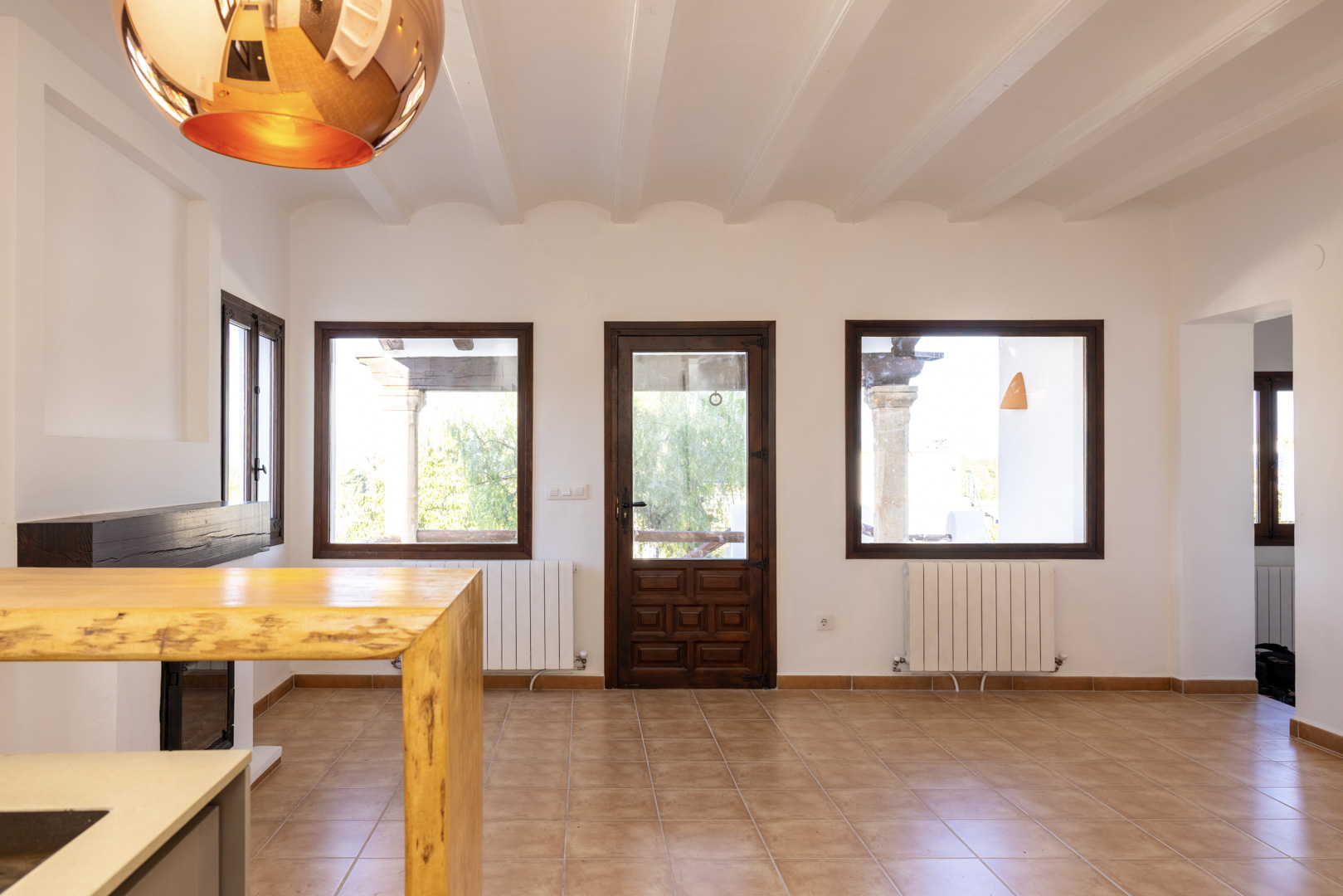 Salon lumineux avec carrelage, poutres apparentes et boiseries foncées. Vues sur l'extérieur.