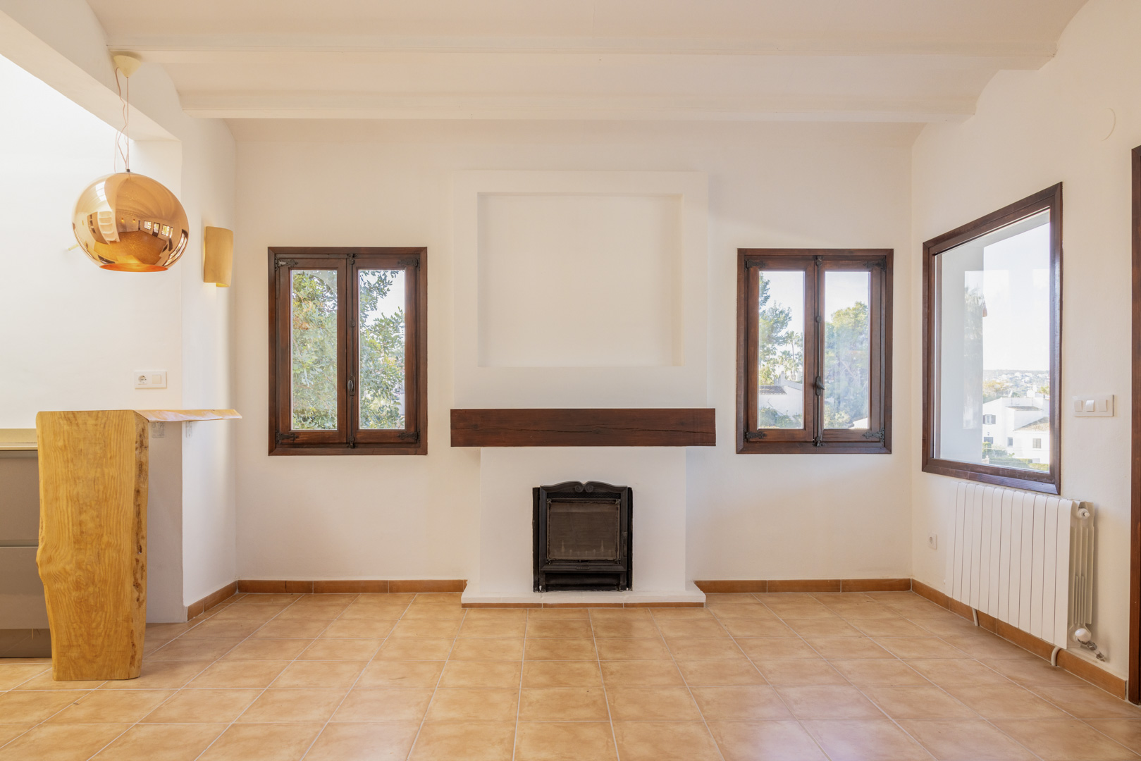 Salon lumineux avec cheminée rustique, fenêtres à cadre en bois et carrelage. Design méditerranéen avec touches modernes.