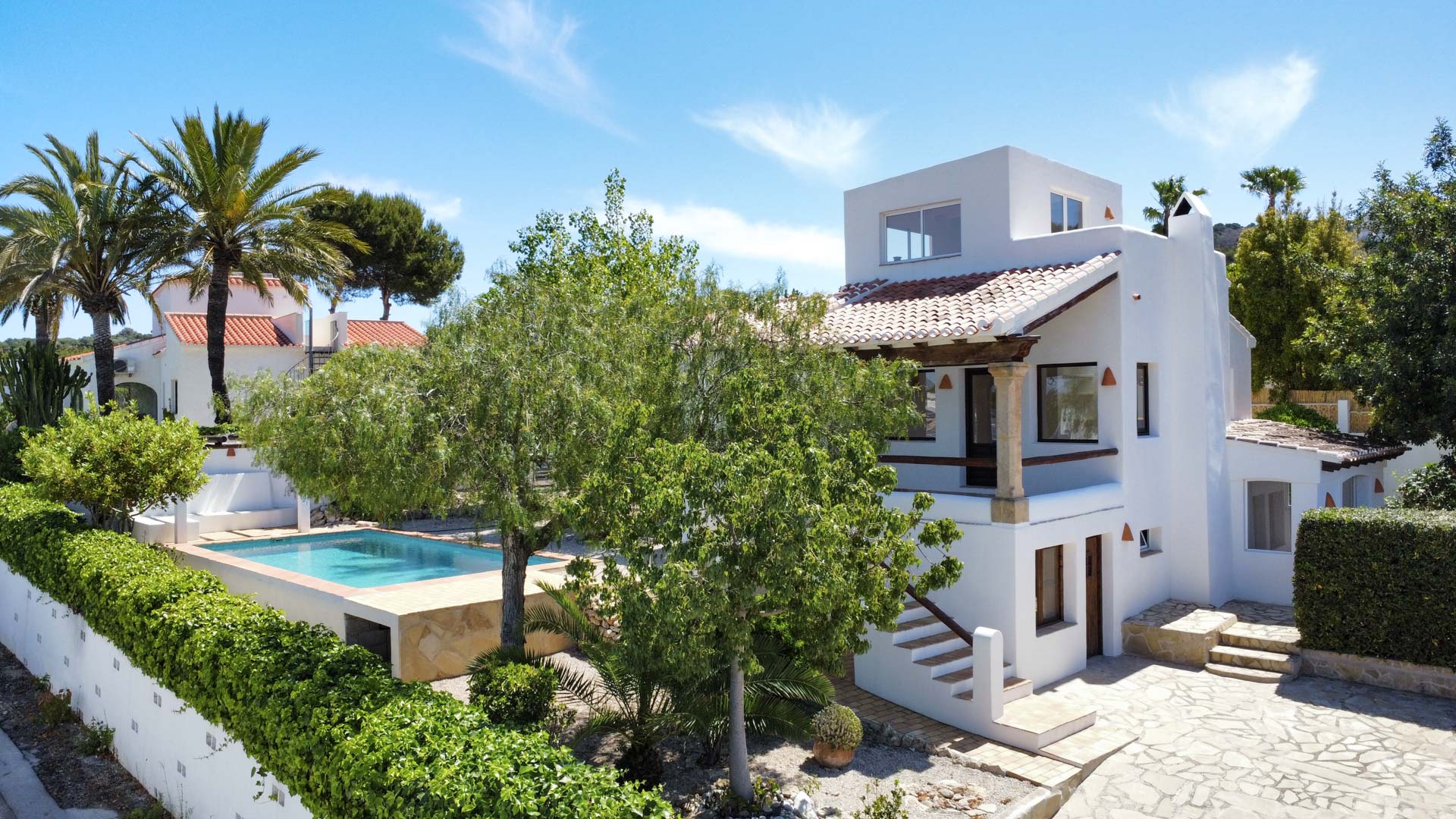 Vue extérieure de la villa avec piscine, jardin et façade blanche. Détails en pierre et végétation luxuriante.