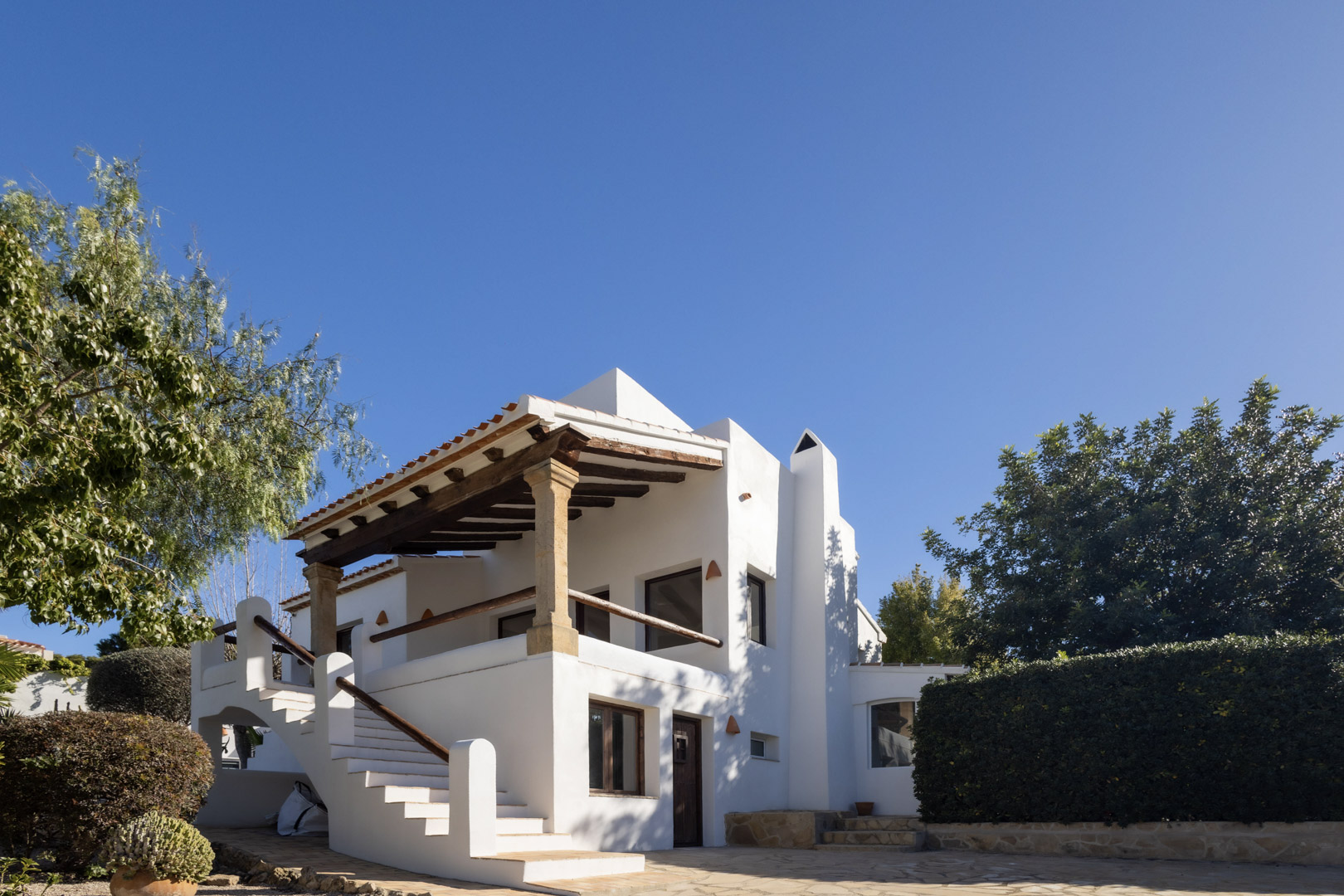 Vue extérieure de la villa rénovée, mettant en valeur l'architecture espagnole traditionnelle et la terrasse couverte avec des poutres en bois.