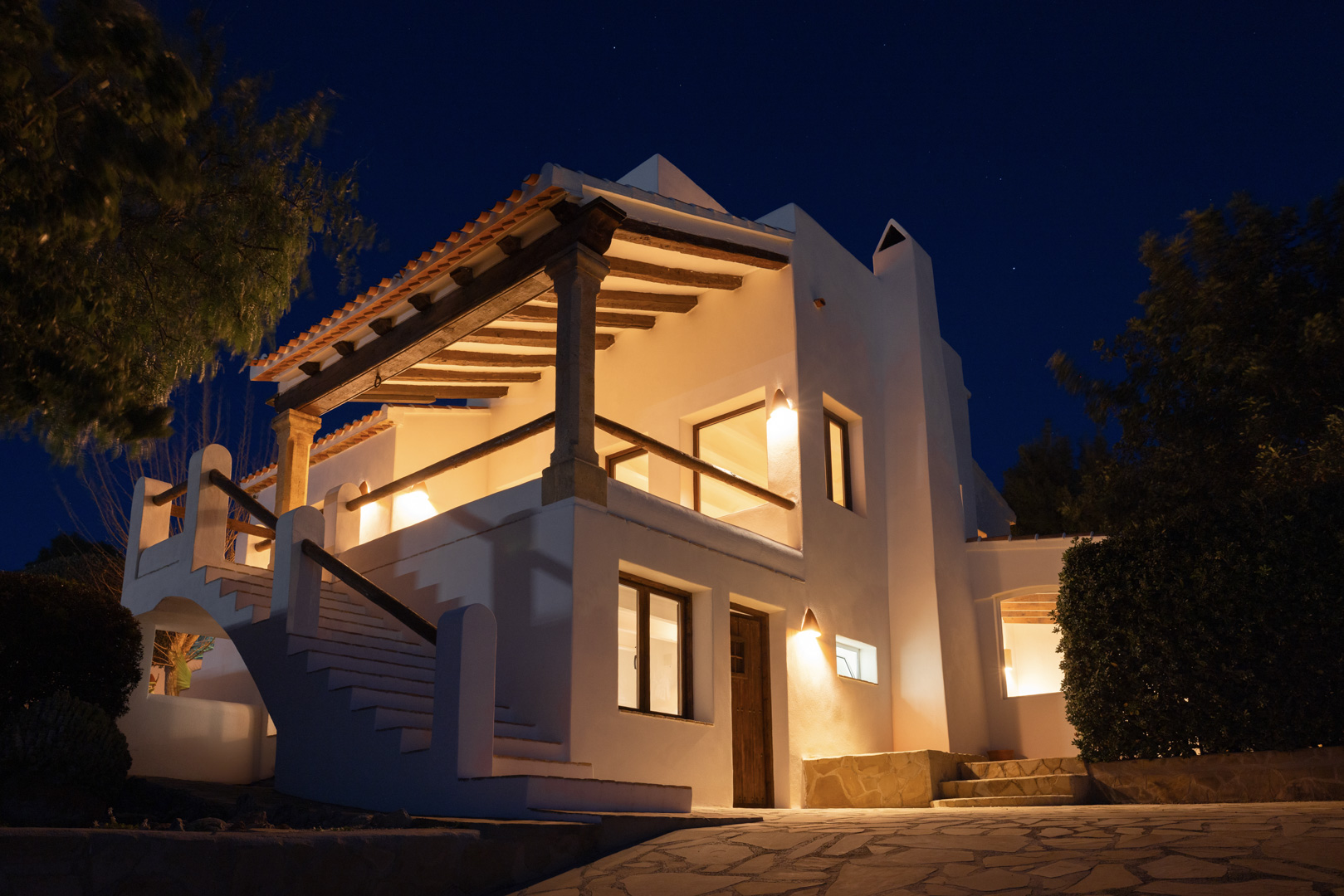 Vue nocturne d'une villa à Tosalet, Jávea. Architecture méditerranéenne avec terrasse couverte, éclairage chaleureux et détails en pierre.