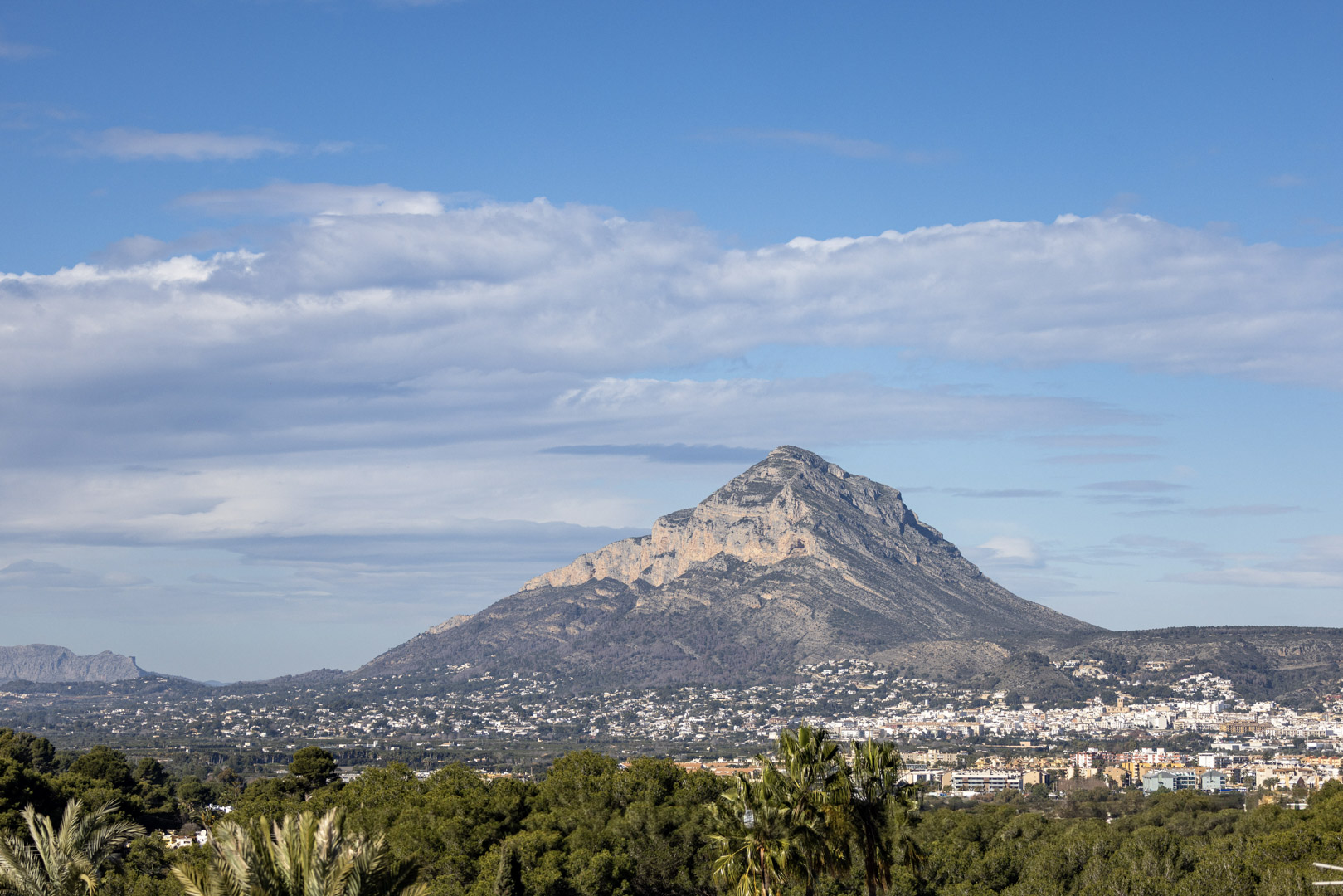 Vue panoramique du Montgó, Jávea, avec un ciel partiellement nuageux et de la végétation au premier plan.