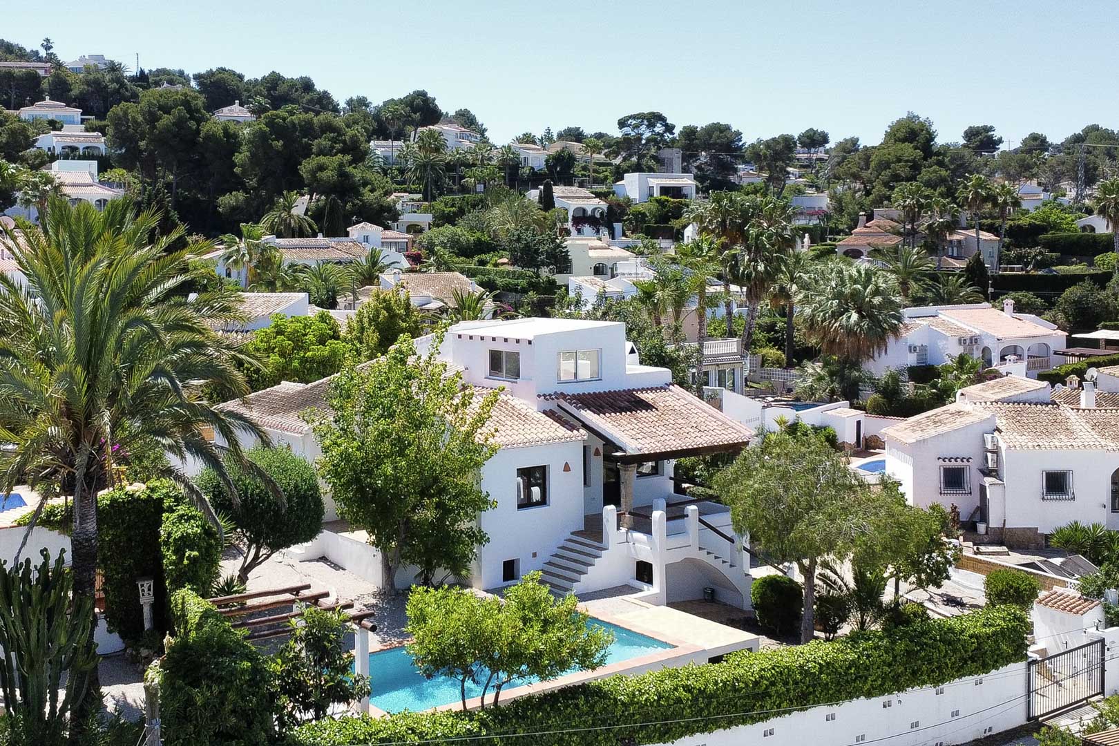Vue surélevée d'une villa blanche avec piscine turquoise et toit de tuiles, nichée dans la verdure à Jávea.