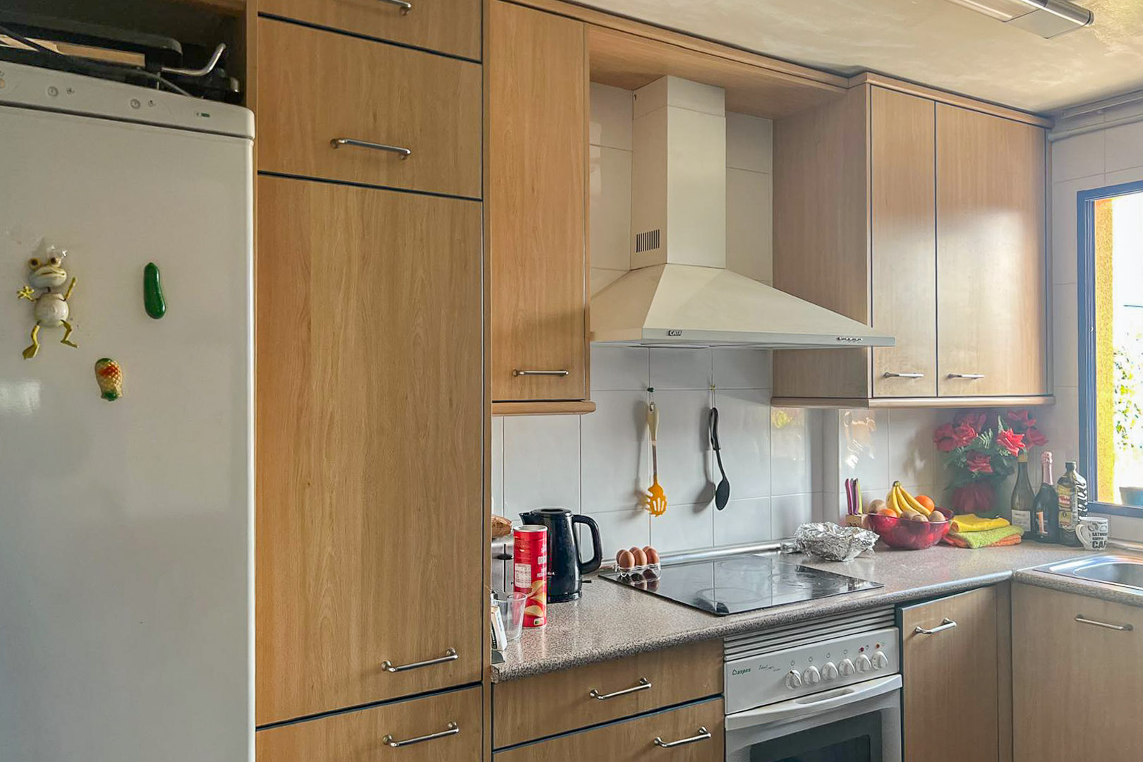 Cuisine fonctionnelle avec armoires en bois clair, électroménagers blancs et plan de travail en granit.