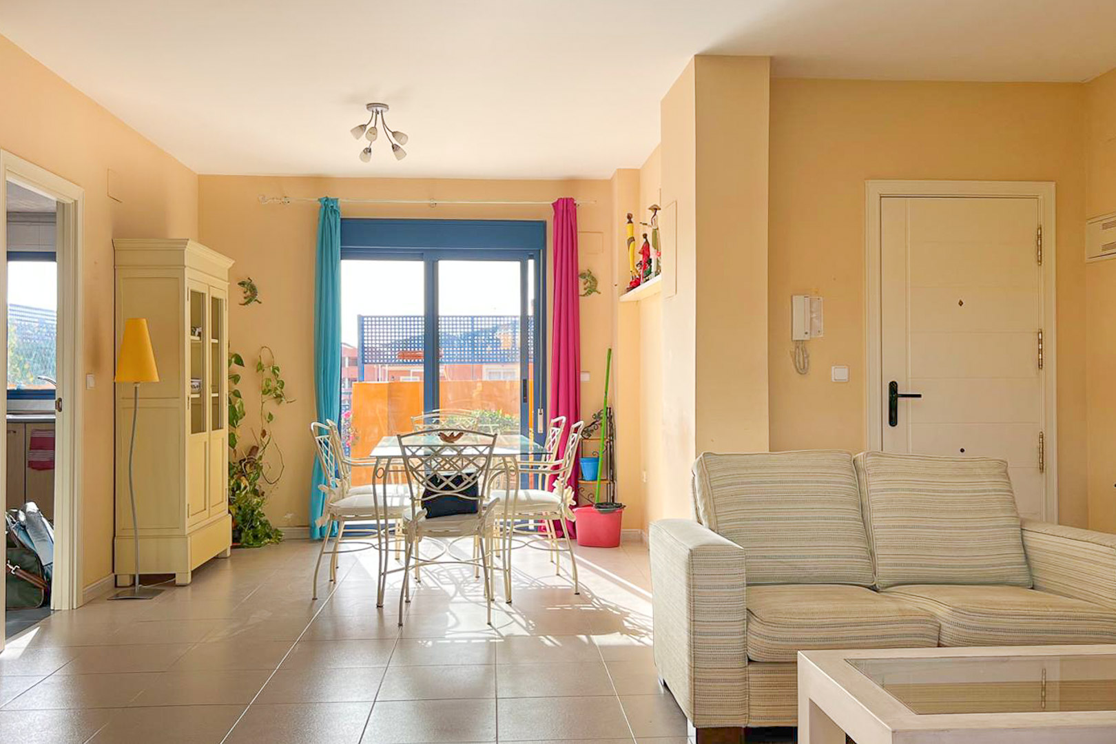 Salon-salle à manger lumineux avec balcon, table à manger en métal et canapé rayé neutre.