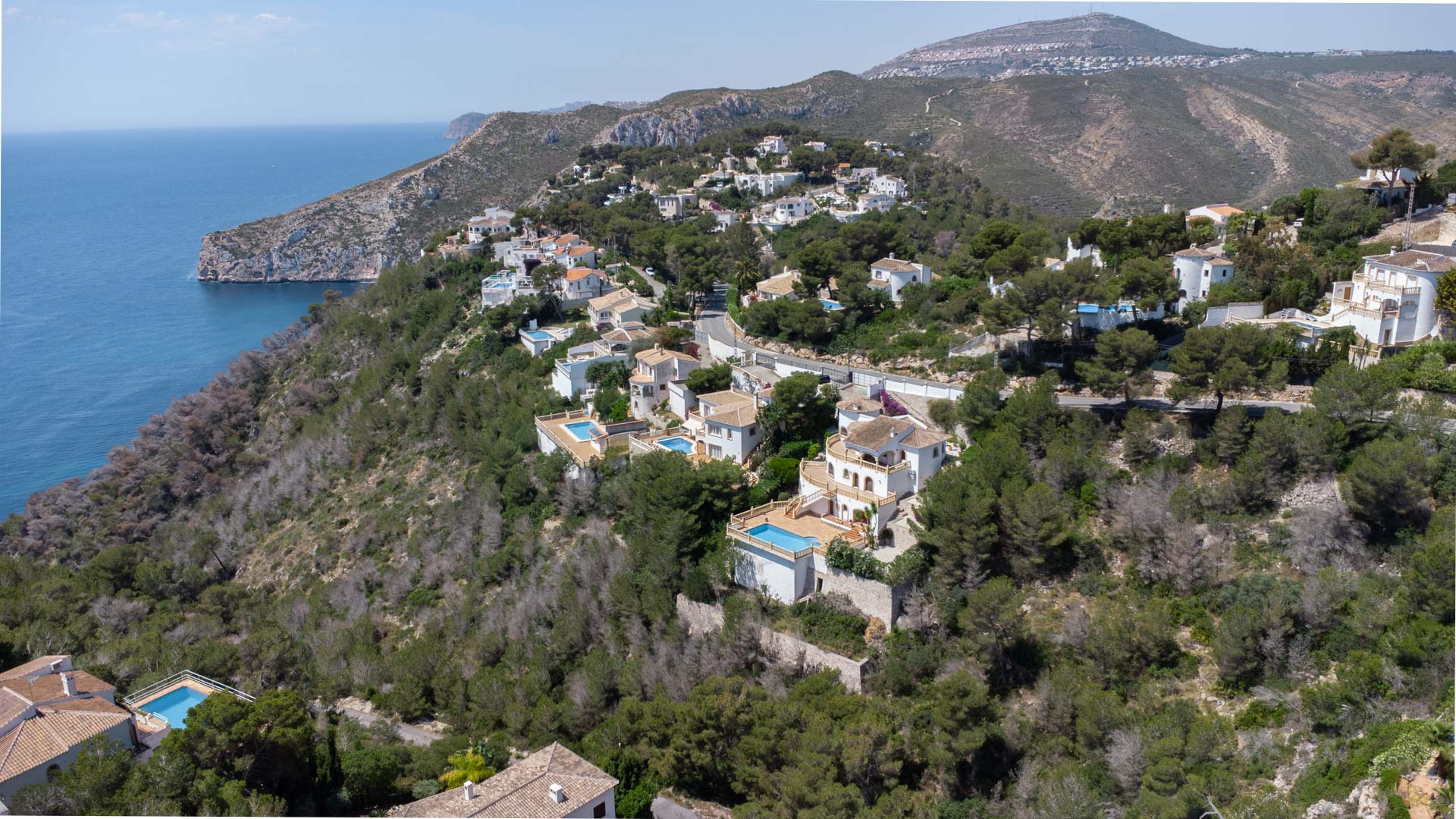 Vue aérienne de la côte de Jávea montrant des villas résidentielles nichées sur une colline boisée surplombant la mer Méditerranée et les falaises.