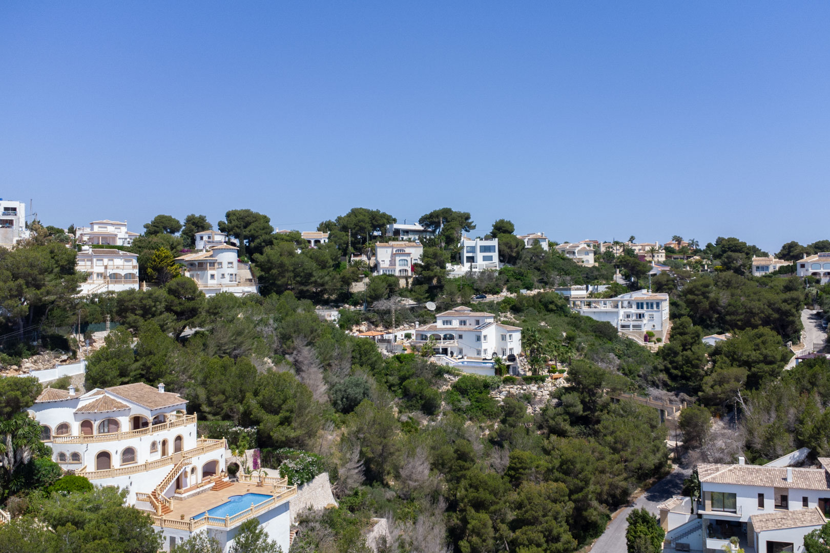 Vue aérienne du quartier résidentiel Costa Nova à Jávea, présentant des villas méditerranéennes avec piscines nichées dans une colline boisée de pins.