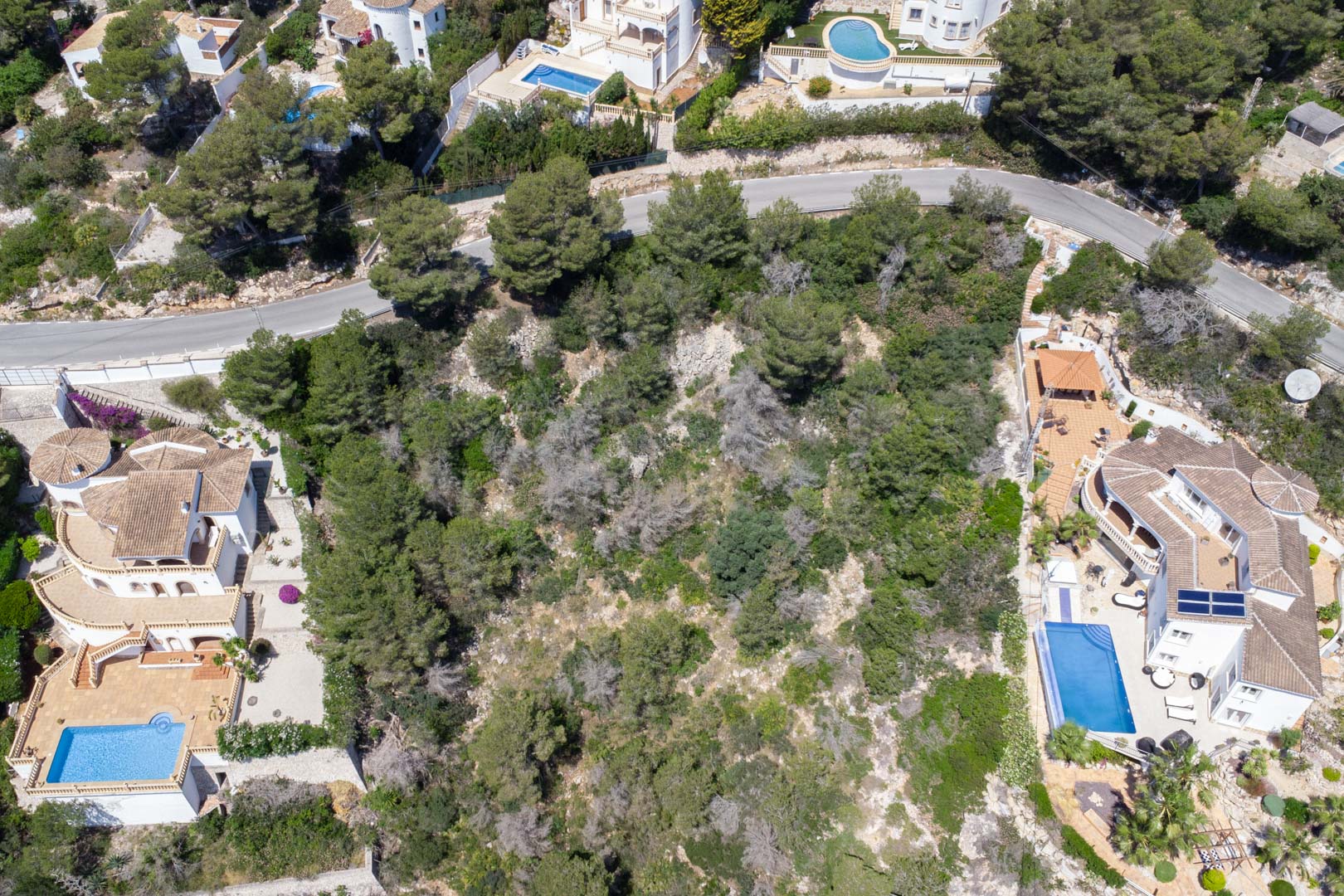 Vue aérienne du terrain en pente avec végétation méditerranéenne, situé entre des villas résidentielles avec piscines privées à Costa Nova.