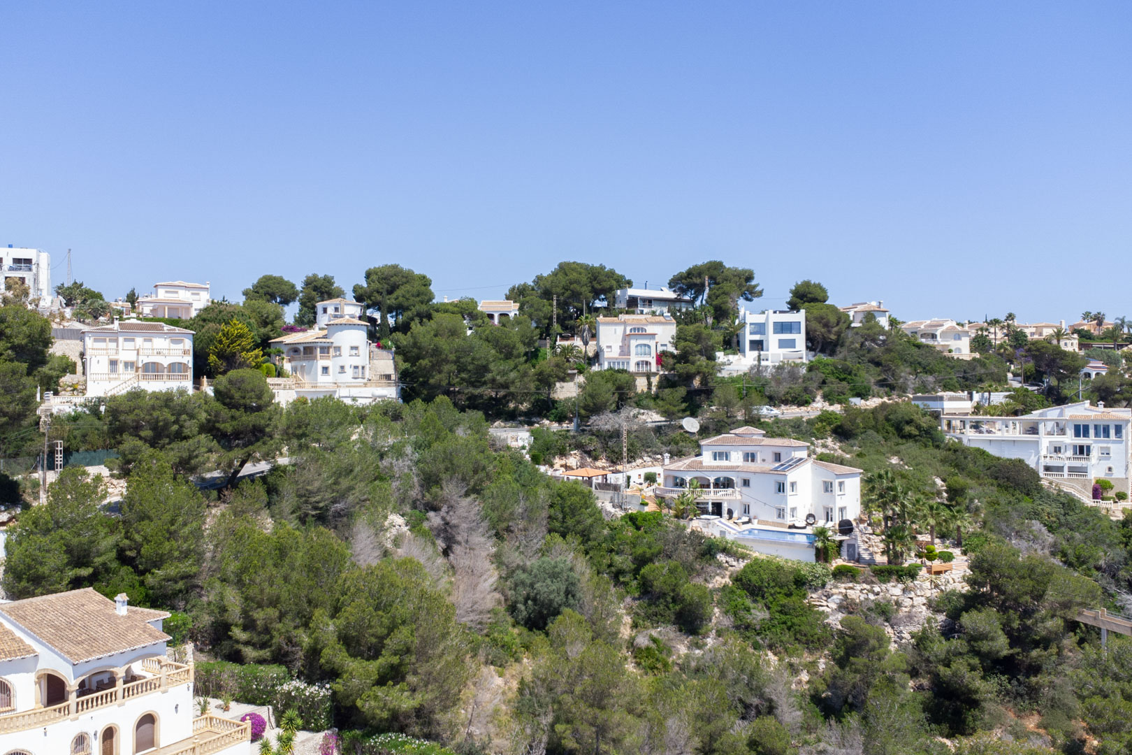 Vue surélevée du quartier résidentiel de Costa Nova à Jávea, avec des villas méditerranéennes nichées dans une colline boisée sous un ciel dégagé.