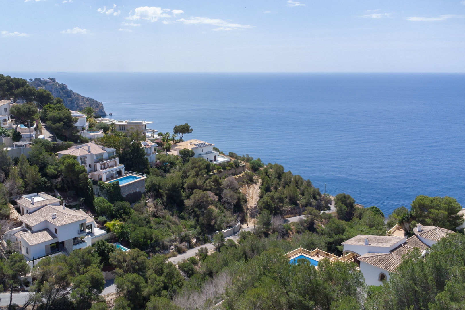 Vue aérienne de la côte de Jávea illustrant des villas méditerranéennes nichées dans la pinède avec une vue dégagée sur l'horizon marin.