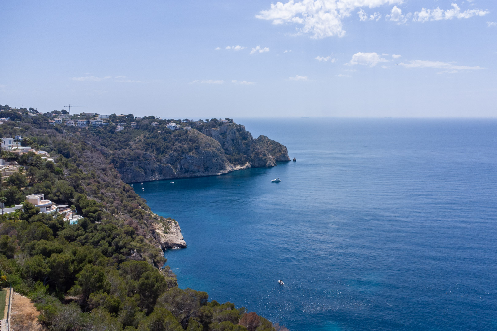 Vue aérienne de la côte escarpée de Jávea, avec des falaises méditerranéennes couvertes de végétation bordant les eaux bleues profondes.