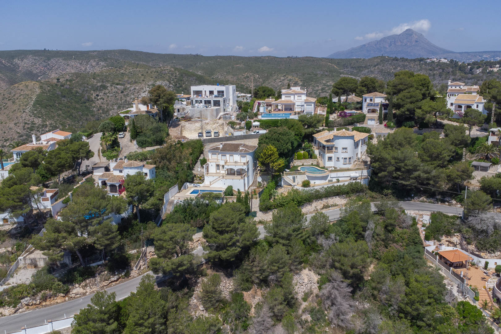 Vue aérienne de l'urbanisation Costa Nova à Jávea, présentant des villas blanches nichées dans les collines boisées avec le mont Montgó à l'horizon.