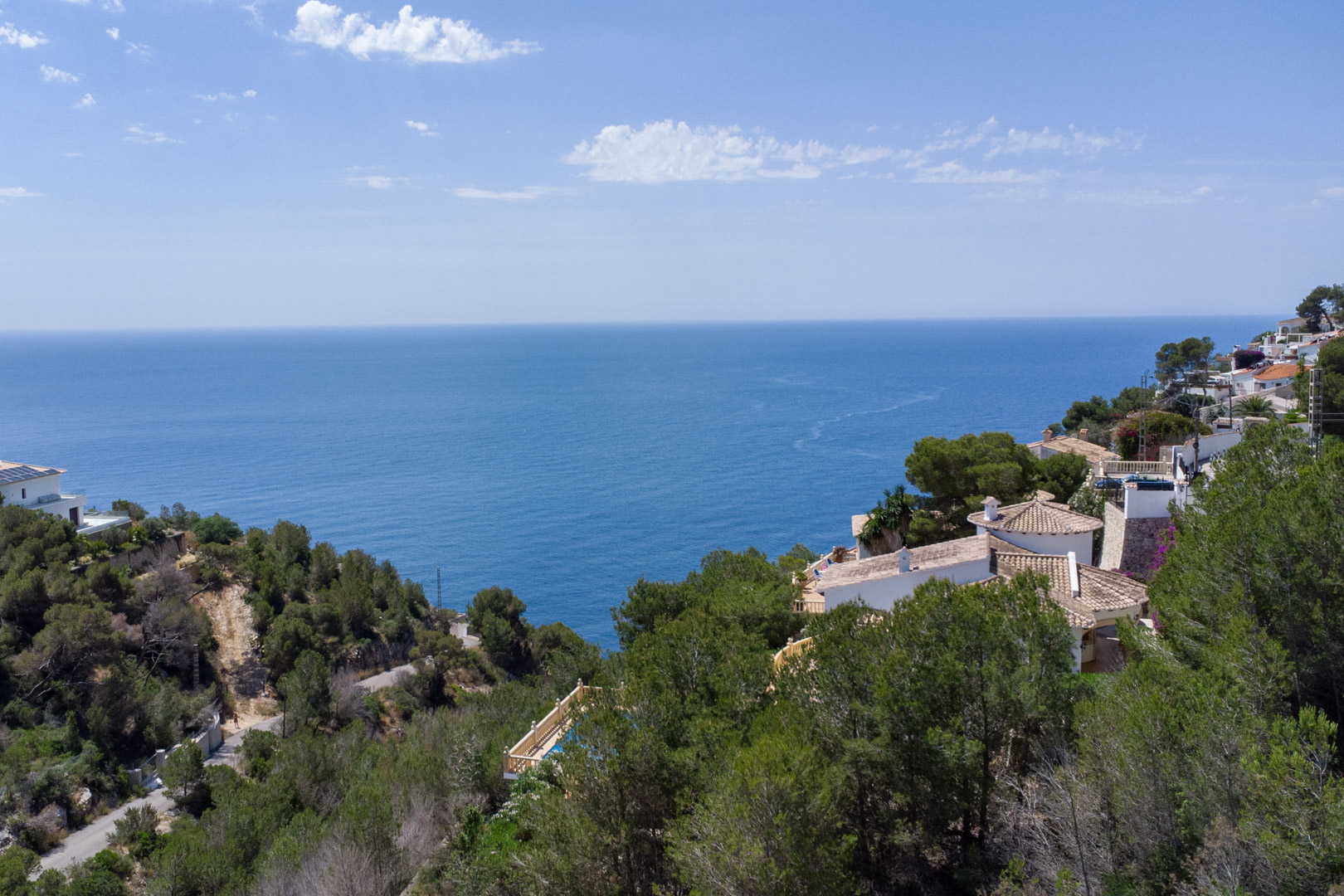 Vue panoramique surélevée de la mer Méditerranée depuis la côte de Jávea, avec des forêts de pins denses et des villas traditionnelles aux toits de tuiles.