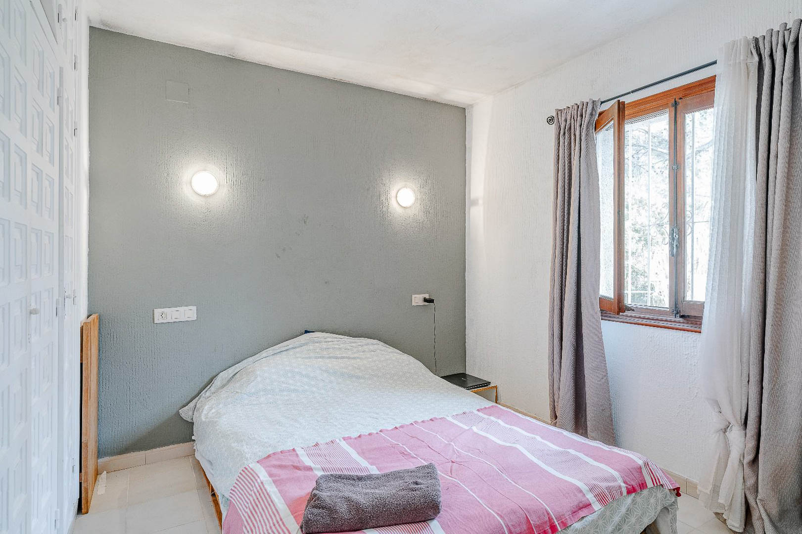 Chambre avec mur d'accent gris, appliques murales circulaires et placard intégré blanc. Fenêtre en bois avec rideaux gris apportant une lumière naturelle.