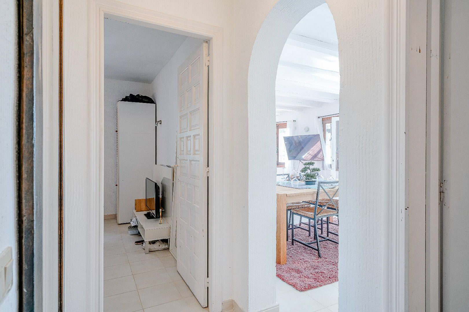 Couloir de distribution avec une arche méditerranéenne menant à la salle à manger et une porte blanche ouvrant sur une chambre lumineuse.
