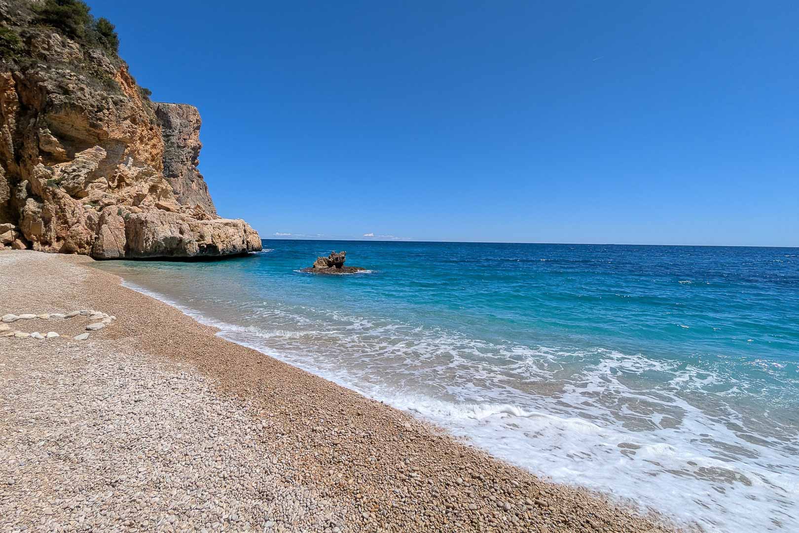La Cala Llebeig, une crique sauvage de galets aux eaux turquoise bordée de falaises, accessible à pied depuis le quartier de La Arnella.