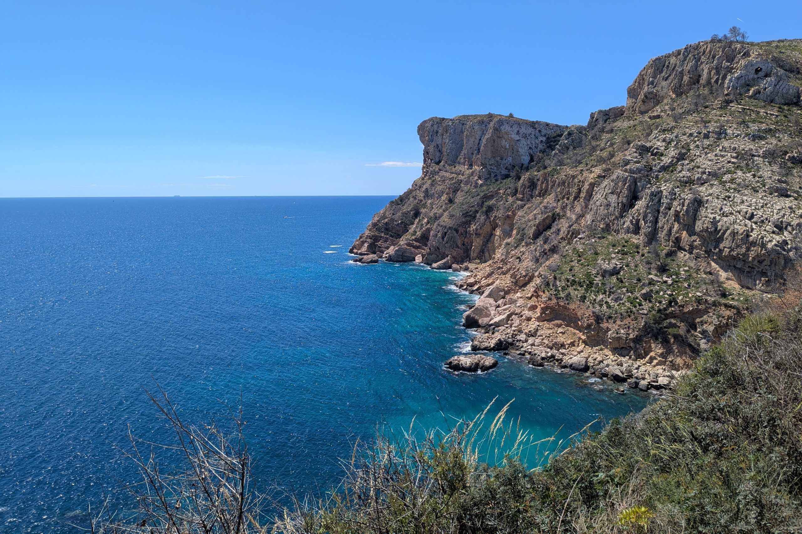 Vue panoramique sur les falaises calcaires et les eaux turquoise de la Méditerranée près de Cala Llebeig, entourées d'une végétation côtière sauvage.