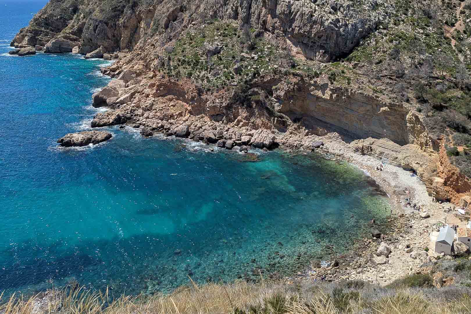 Vue sur la Cala Llebeig aux eaux turquoise et falaises escarpées, accessible par un sentier situé à proximité immédiate de l'arrière du terrain.
