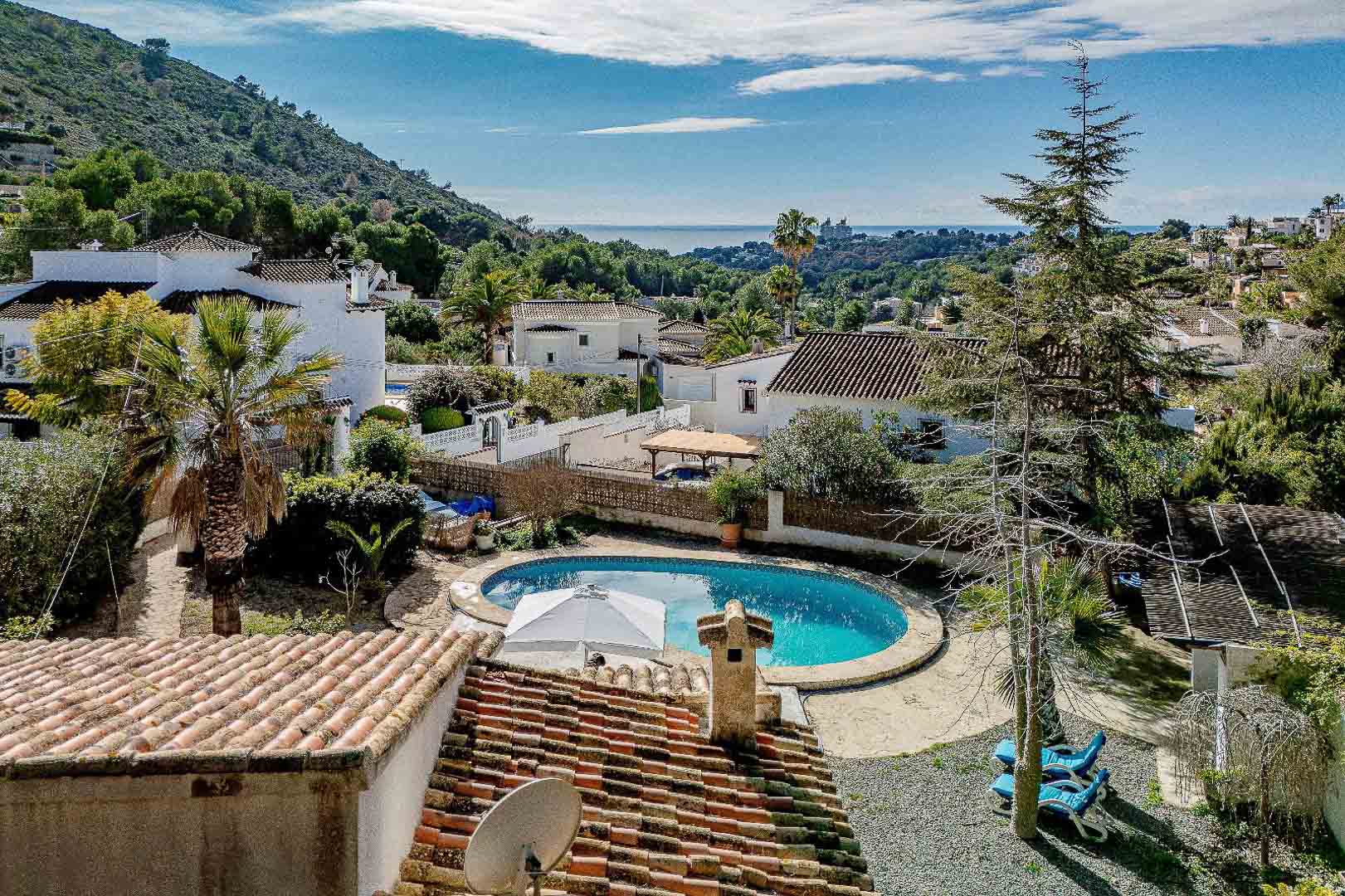 Vue surélevée de la piscine privée en forme de rein et du jardin méditerranéen, avec un panorama sur la mer et les collines environnantes de Moraira.