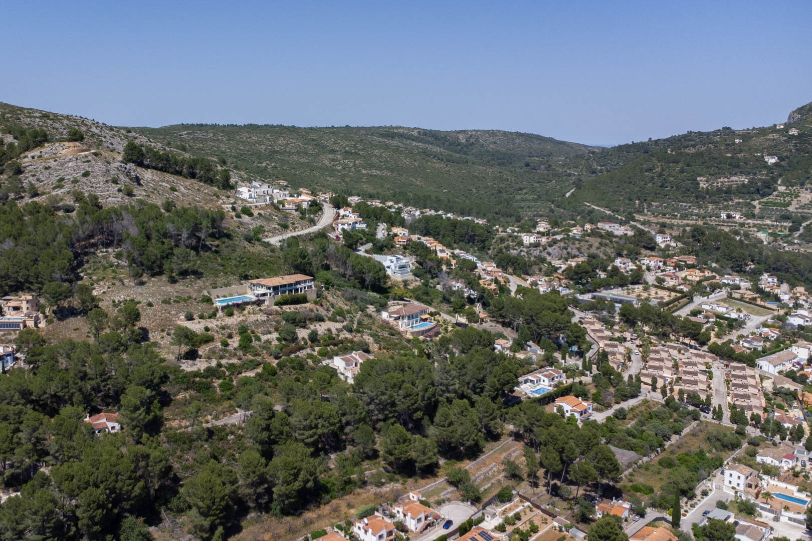 Vue aérienne du Residencial VALL DE POP à Alcalalí, illustrant l'emplacement surélevé des parcelles au cœur de la nature avec une vue dégagée sur la vallée.