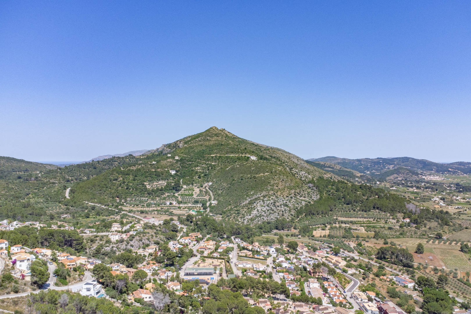 Vue aérienne panoramique de la vallée de Jalón et du village d'Alcalalí, mettant en valeur le paysage montagneux méditerranéen et l'environnement naturel préservé.