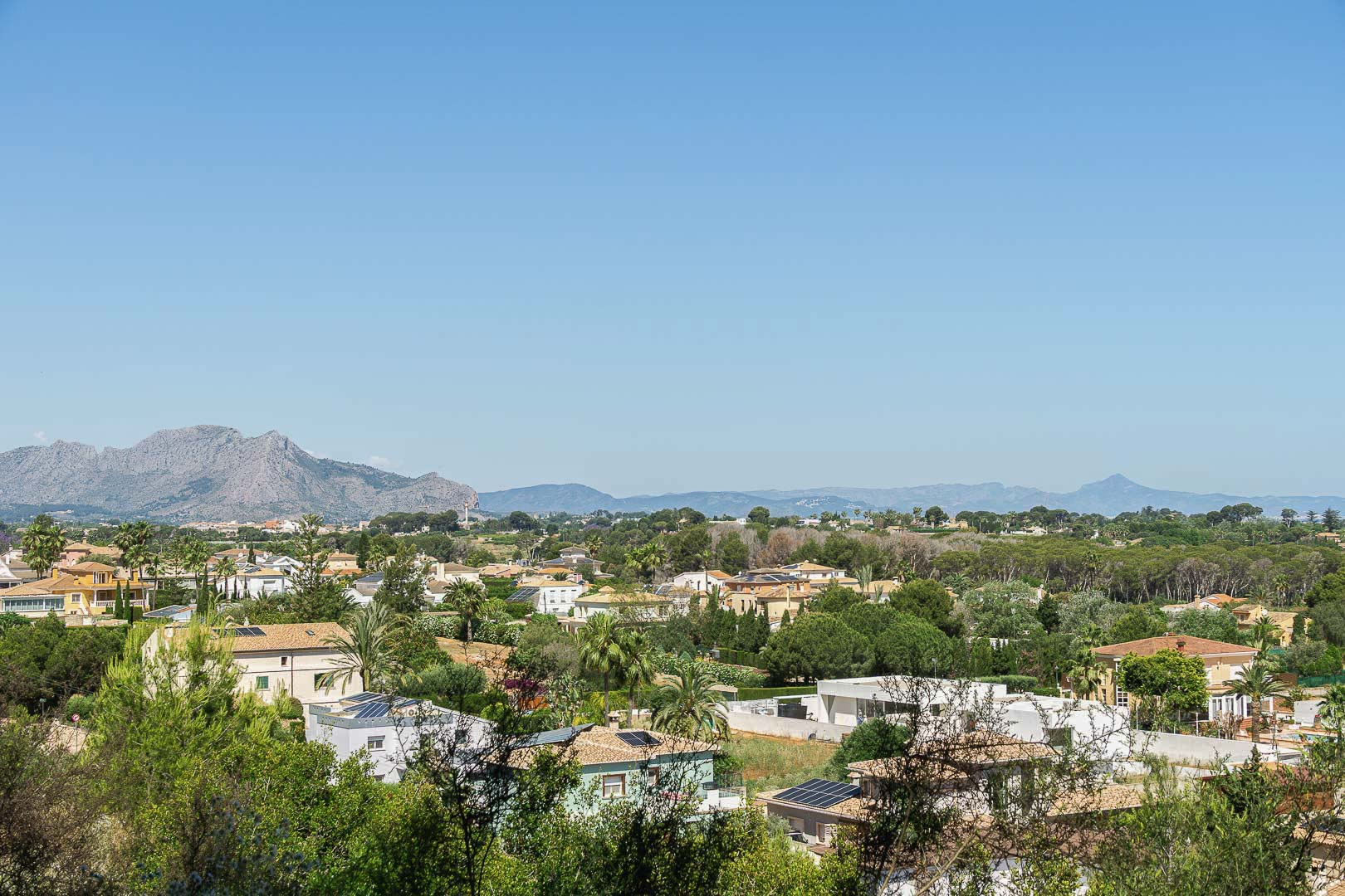 Vue panoramique de Dénia avec maisons, verdure et montagnes en arrière-plan.