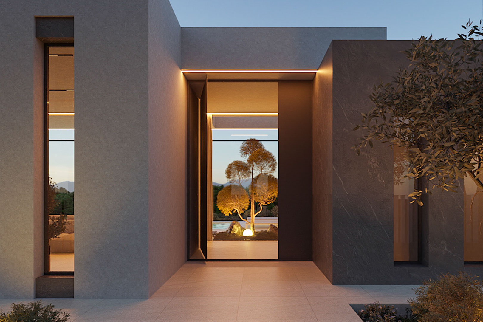 Entrée principale minimaliste avec façade en pierre grise, éclairage LED intégré et vue sur le jardin intérieur et ses oliviers éclairés.