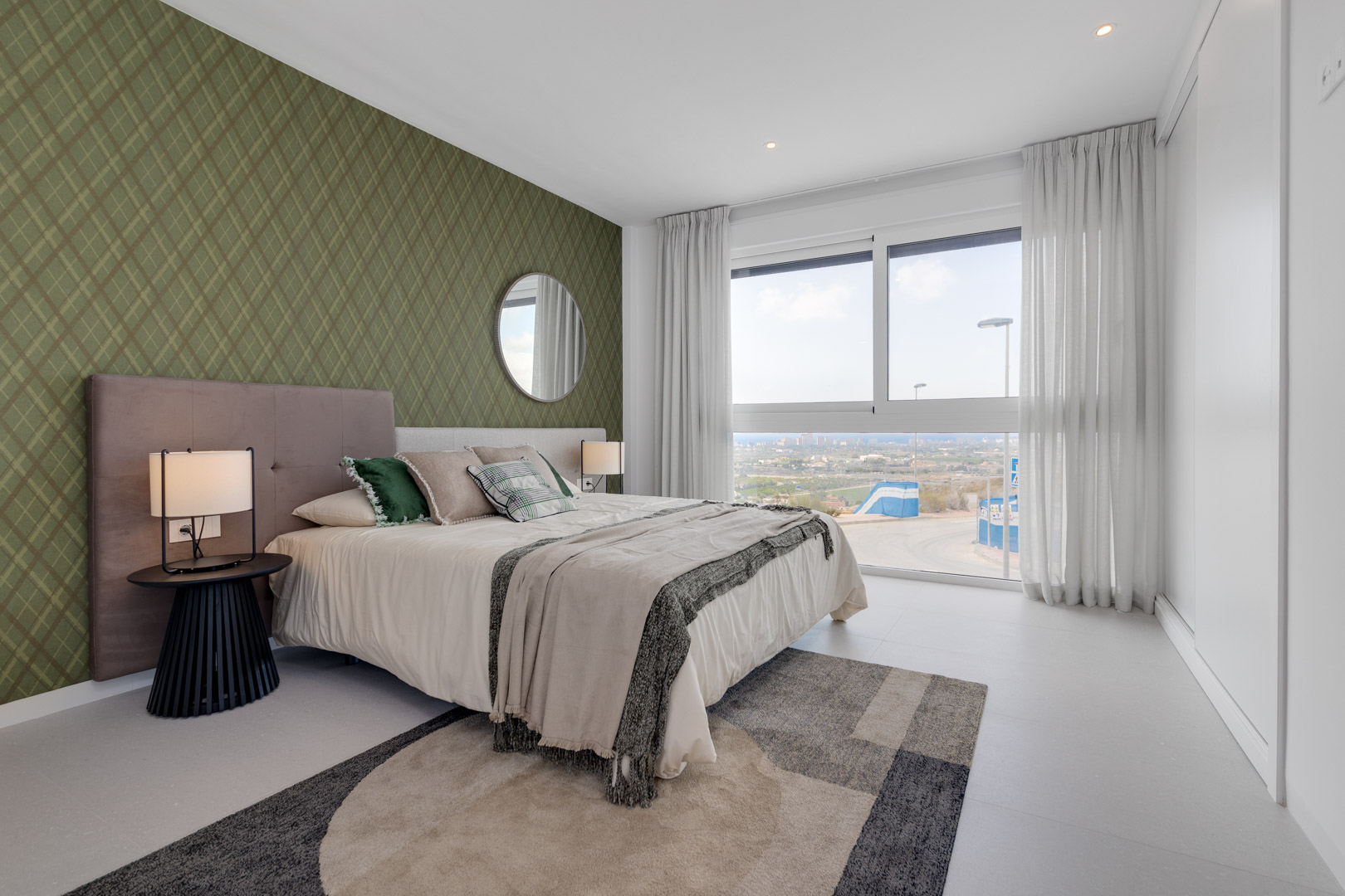 Chambre avec mur d'accent vert à motifs, grande baie vitrée offrant une vue dégagée et placards intégrés blancs. Éclairage encastré et sol en grès cérame.