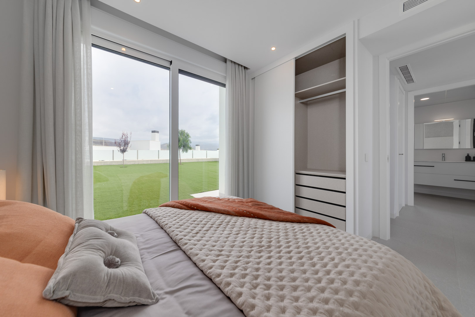 Chambre avec placard intégré, baies vitrées offrant un accès direct au jardin et vue sur la salle de bain attenante avec meuble vasque moderne.