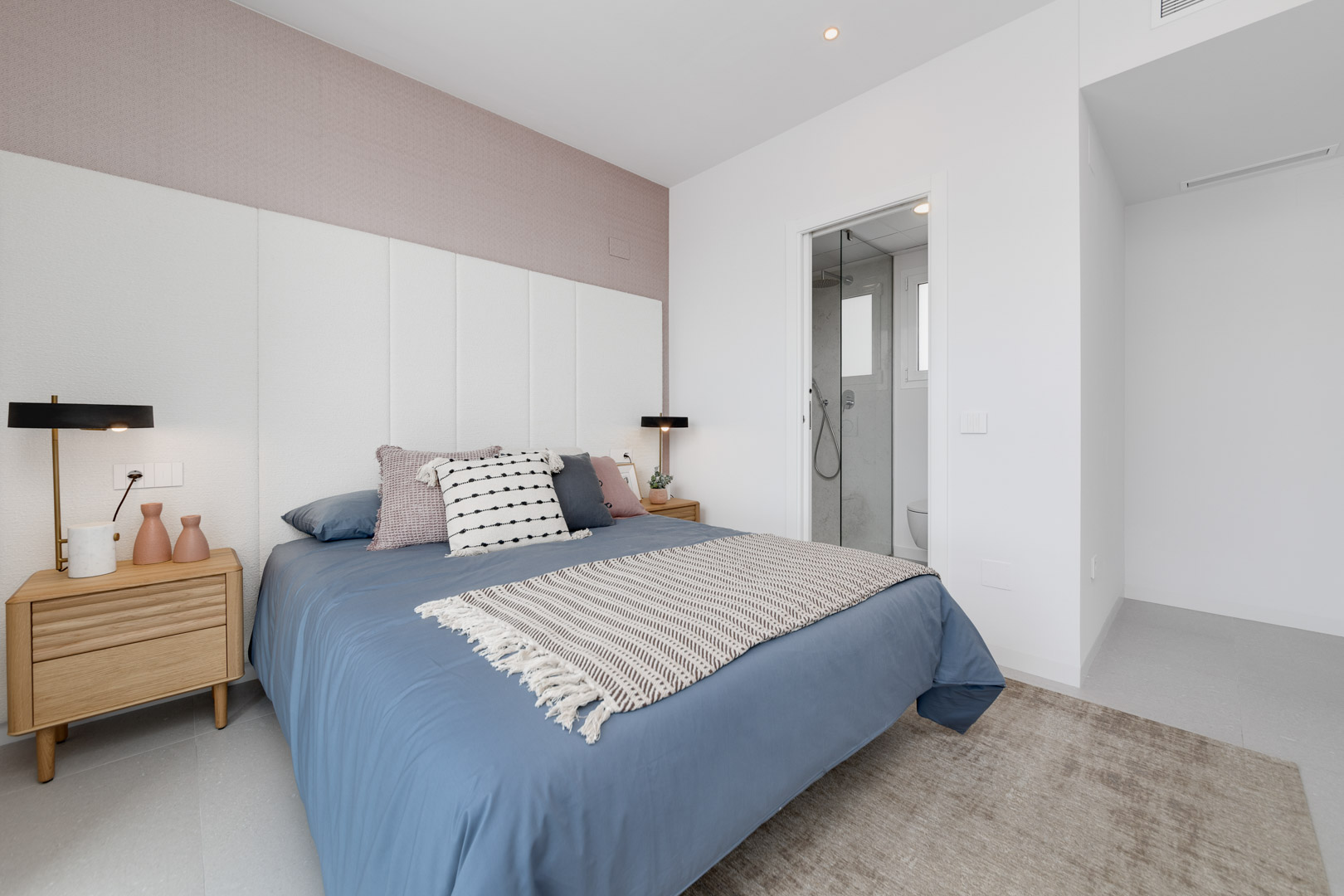 Chambre contemporaine avec tête de lit à panneaux blancs, mur d'accent mauve et salle de bain attenante avec paroi en verre.