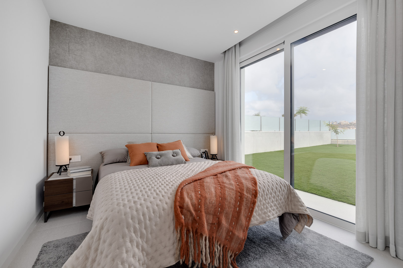 Chambre contemporaine avec tête de lit rembourrée, textiles aux tons terre et grandes baies vitrées offrant un accès direct au jardin privé.