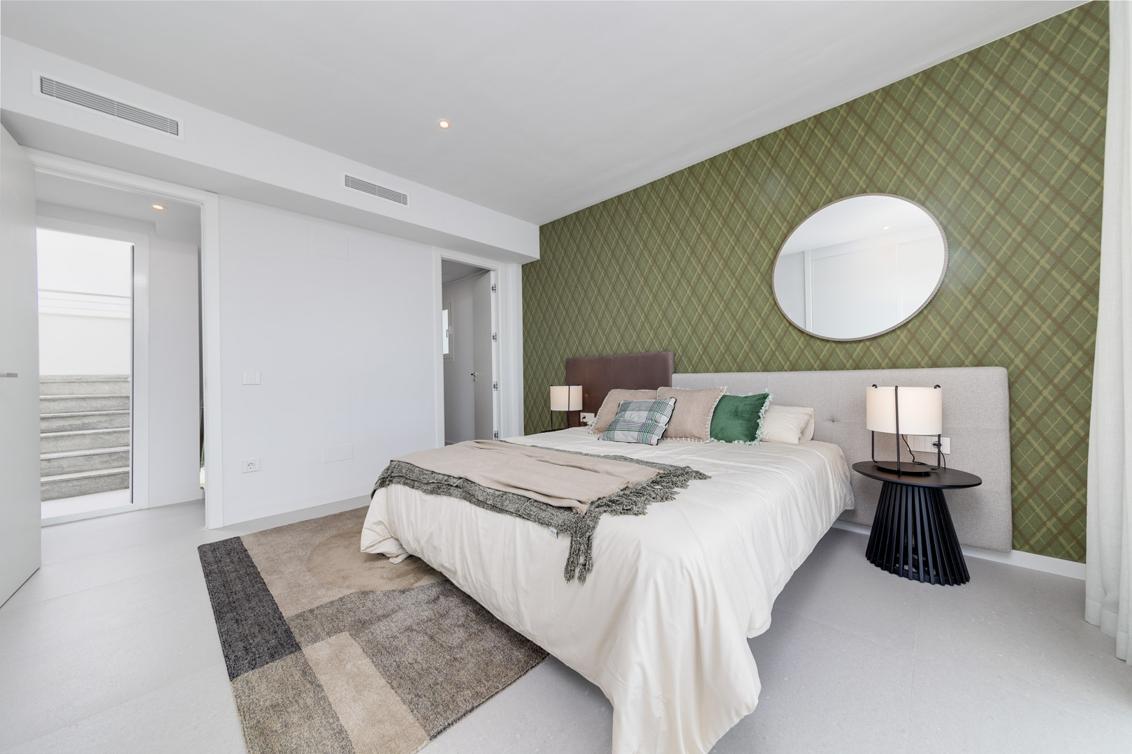 Chambre contemporaine avec un mur d'accent en papier peint vert olive, miroir circulaire et système de climatisation intégré par grilles linéaires.