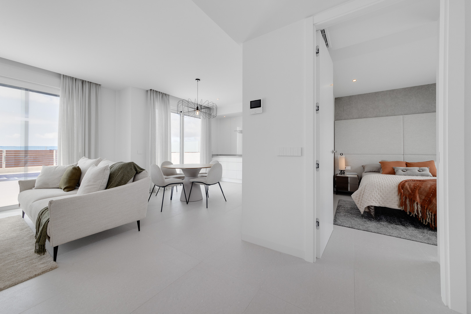 Espace de vie ouvert comprenant un salon élégant, une salle à manger lumineuse et un aperçu d'une chambre aux tons terreux et finitions modernes.