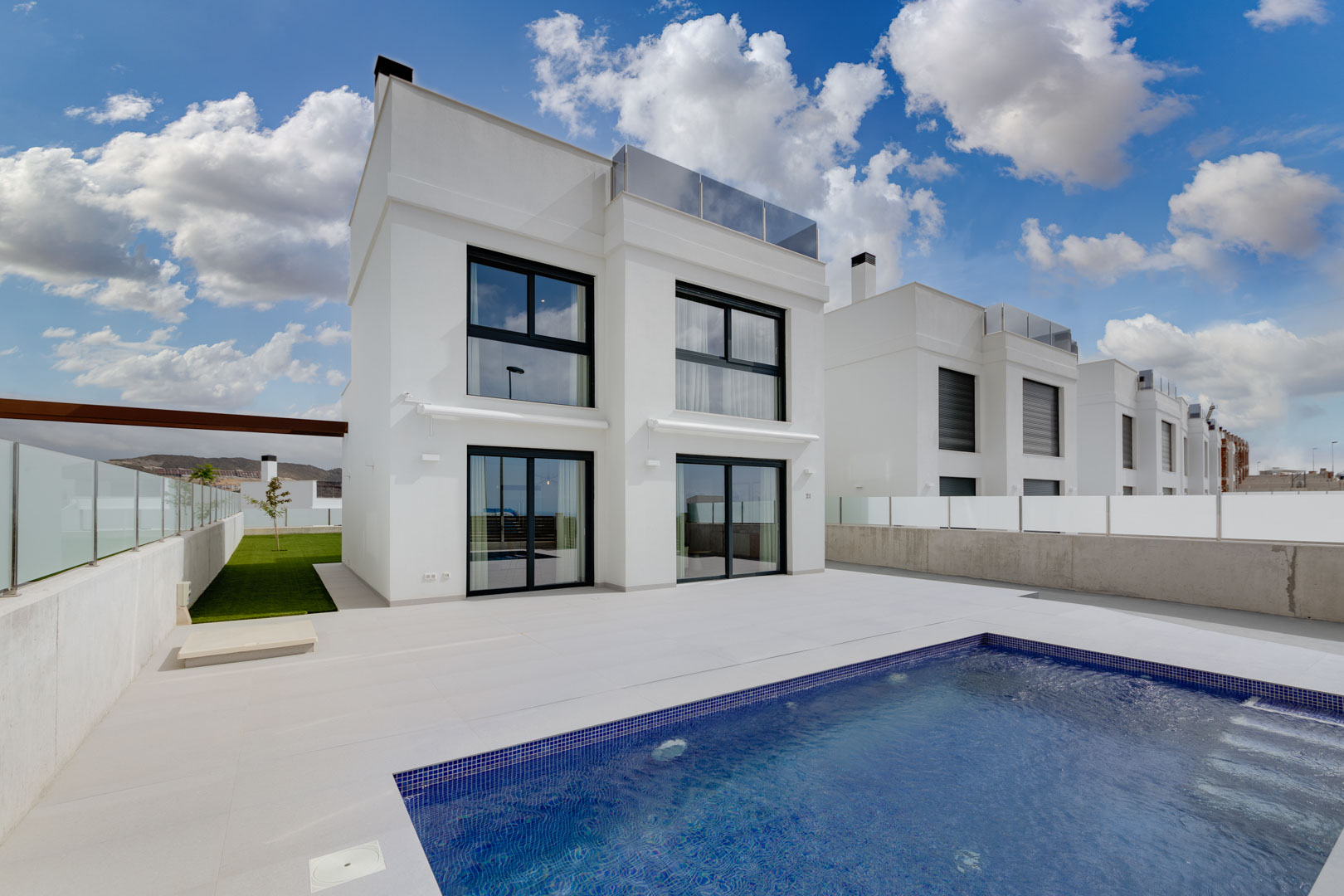 Façade contemporaine blanche aux menuiseries noires, vaste terrasse en grès et piscine privée avec mosaïque bleue.
