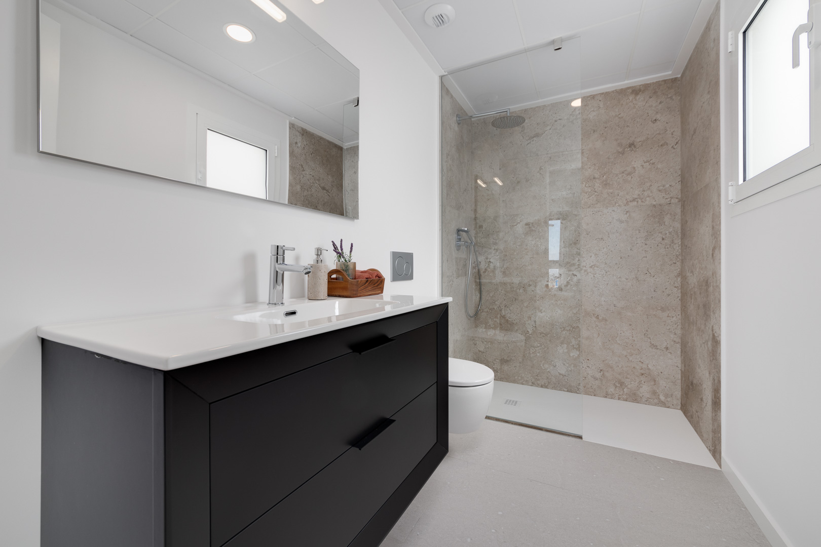Salle de bain moderne avec meuble vasque noir, douche à l'italienne aux parois effet pierre et finitions chromées élégantes.