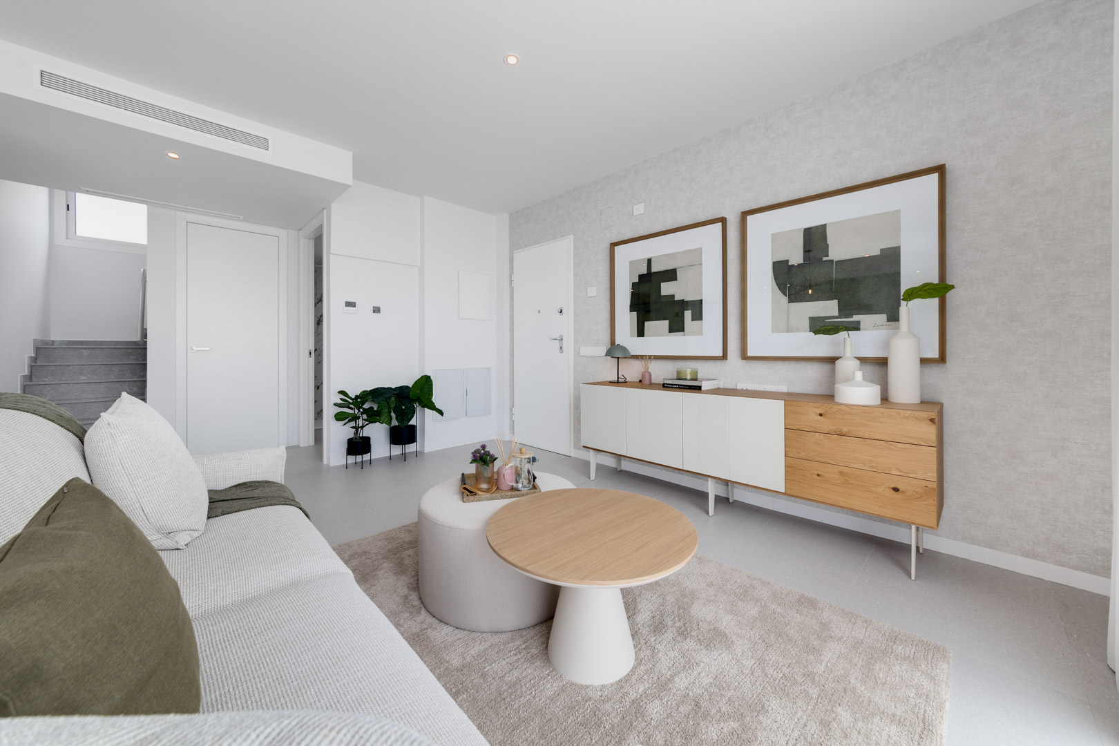 Salon contemporain avec buffet en bois et blanc, œuvres d'art abstraites et espace de détente aux tons neutres avec éclairage encastré.