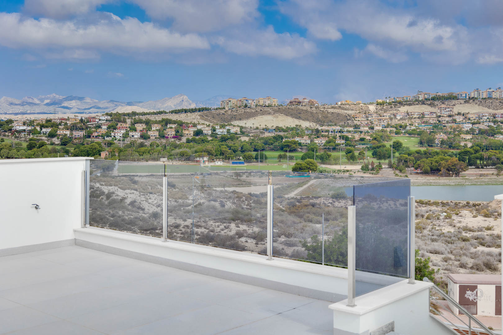 Terrasse supérieure avec carrelage gris et garde-corps en verre, offrant une vue panoramique sur les montagnes, le lac et les parcours de golf.