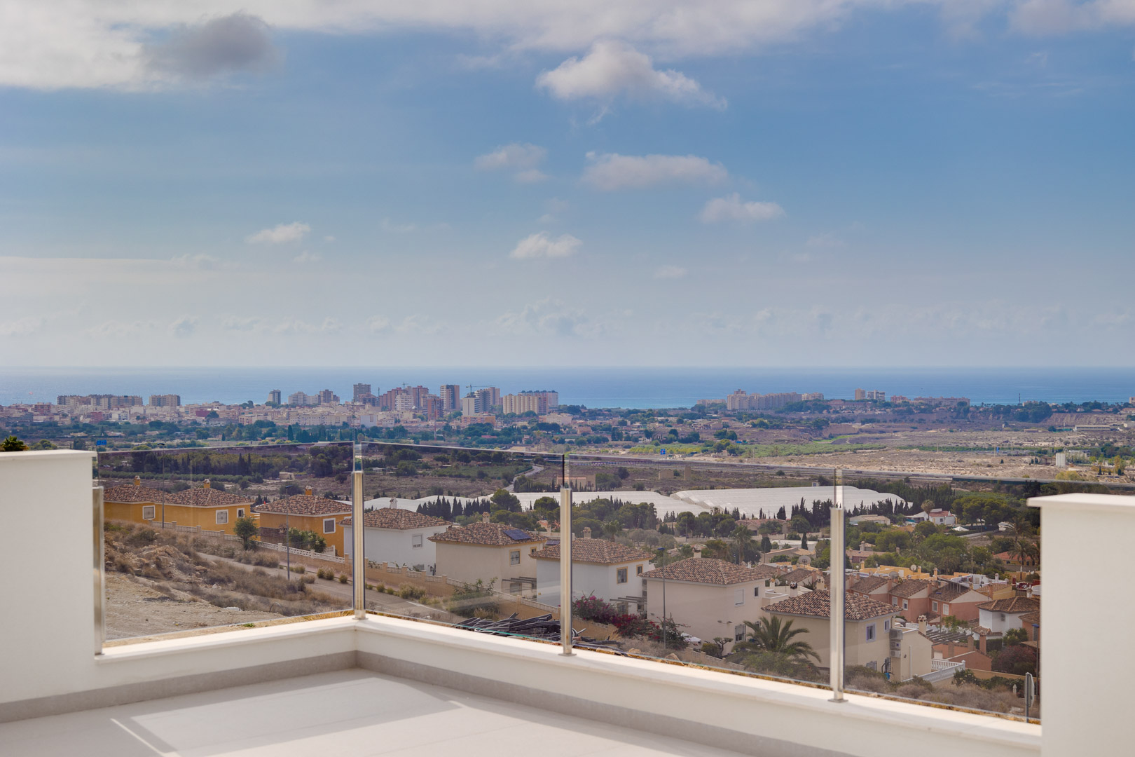 Terrasse supérieure avec revêtement de sol clair et garde-corps en verre, offrant une vue panoramique imprenable sur la côte et la mer Méditerranée.