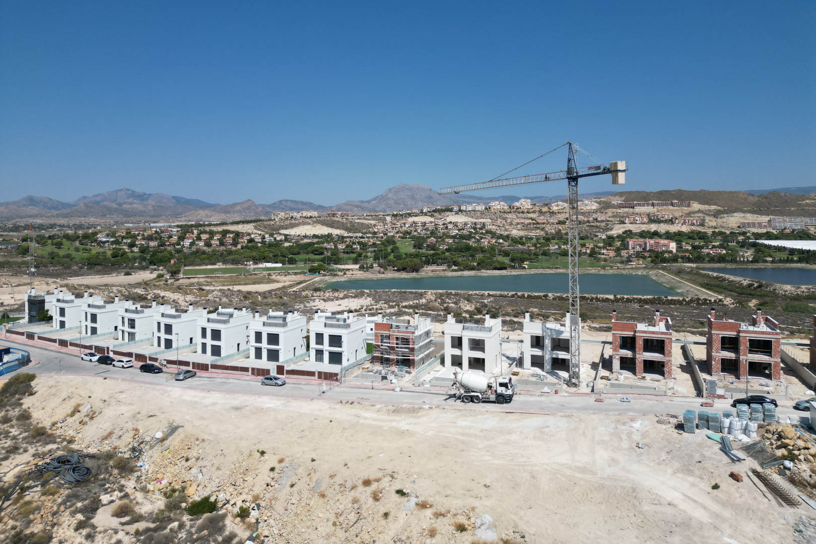 Vue aérienne de l'avancement des travaux des villas contemporaines, illustrant les façades blanches achevées et les structures en briques face au golf et aux montagnes.