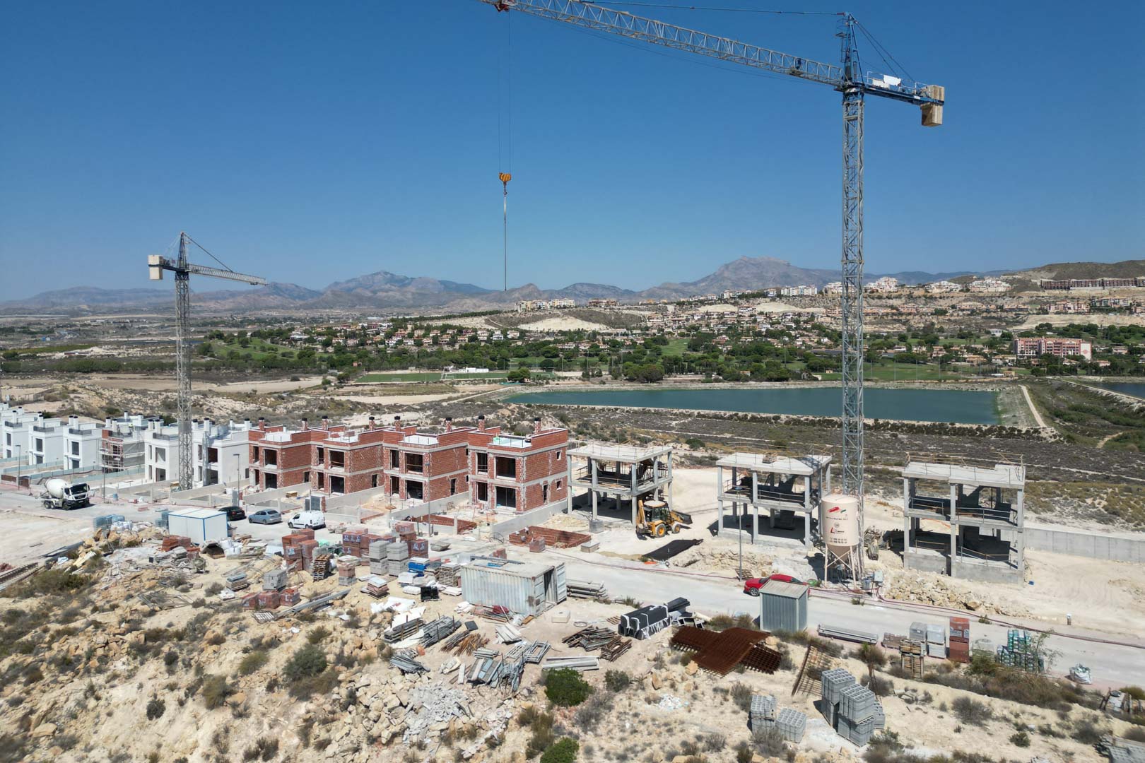 Vue aérienne de l'avancement des travaux des villas, illustrant les structures en briques, les grues et le cadre naturel avec golf et montagnes en arrière-plan.