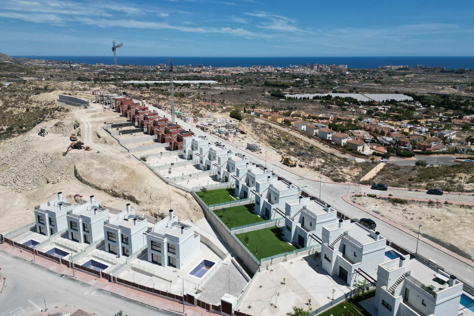 Vue aérienne de villas contemporaines aux façades blanches sur une colline, avec piscines privées, jardins et vue panoramique sur la mer Méditerranée.