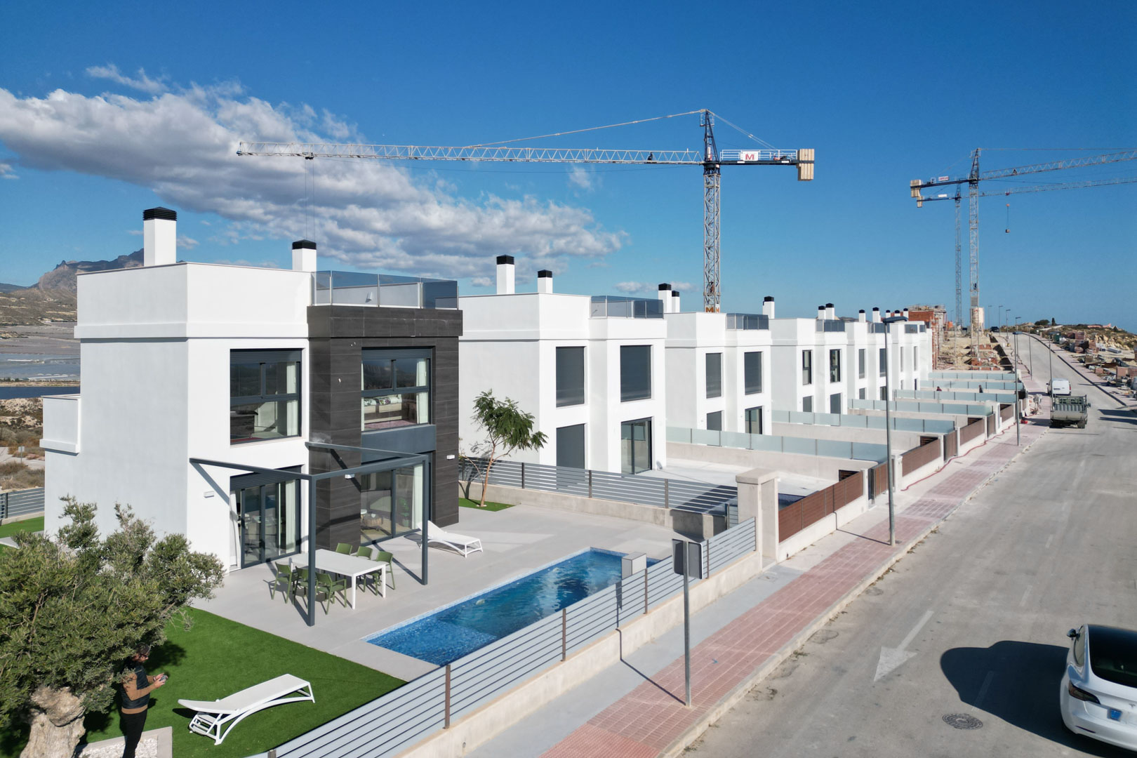 Vue aérienne de villas contemporaines avec façades blanches, accents en pierre, piscines privées, terrasses aménagées et solariums en toiture.