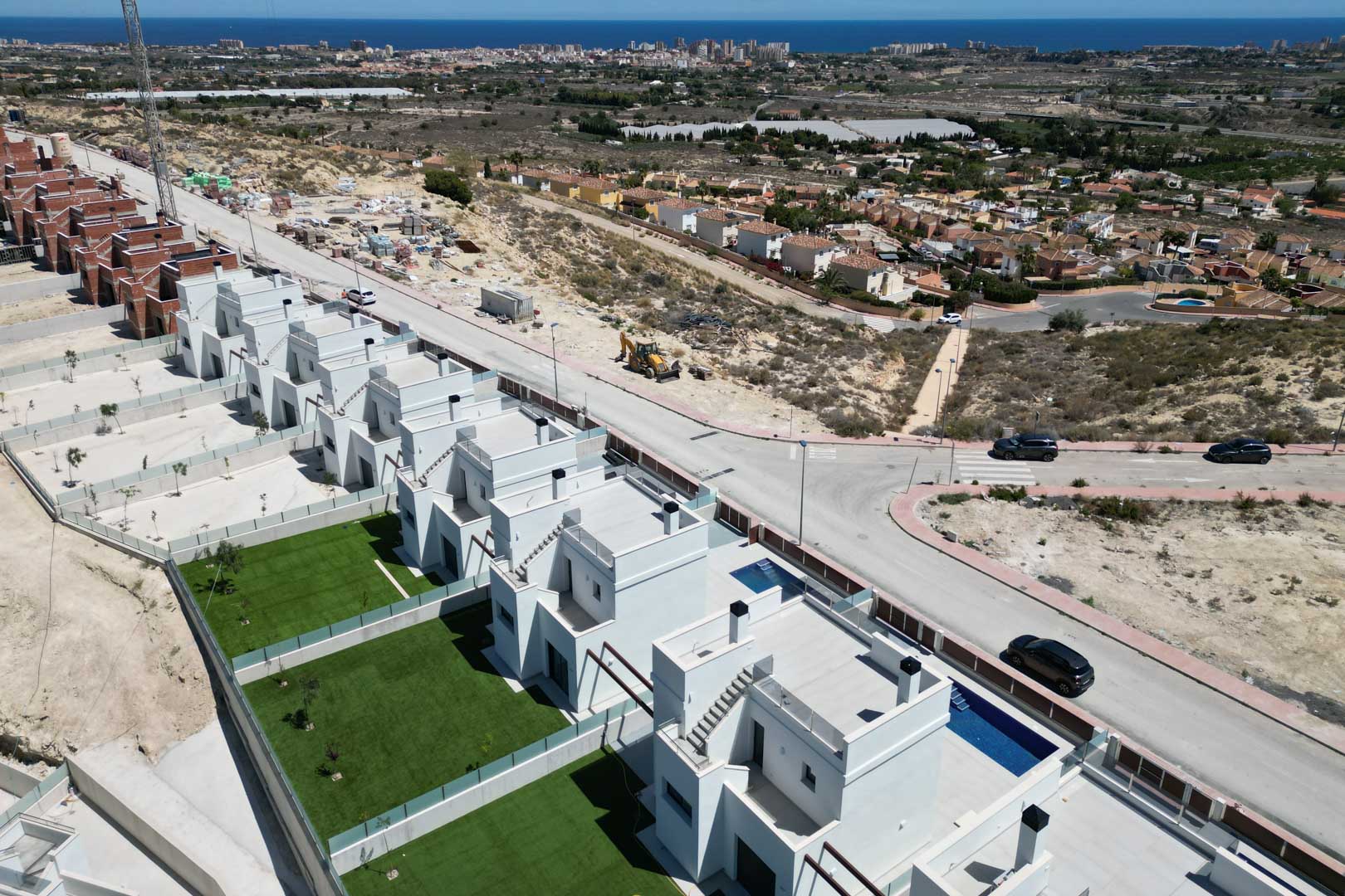 Vue aérienne de villas modernes avec jardins privés, piscines et toits-terrasses, situées sur une colline surplombant le littoral méditerranéen et les environs.