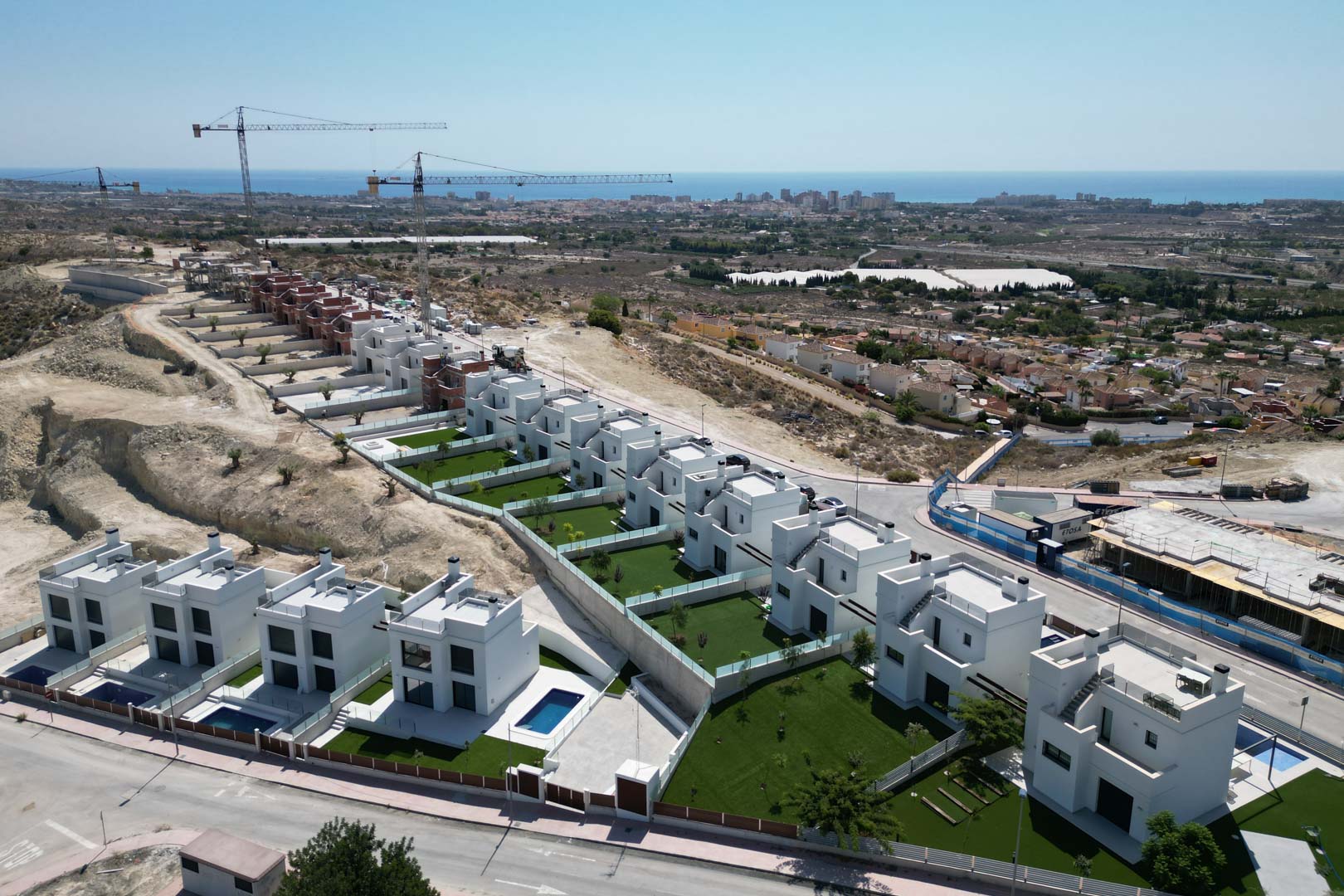 Vue aérienne de villas modernes blanches sur une colline, présentant des jardins privés, des piscines individuelles et une vue surélevée de la côte méditerranéenne.
